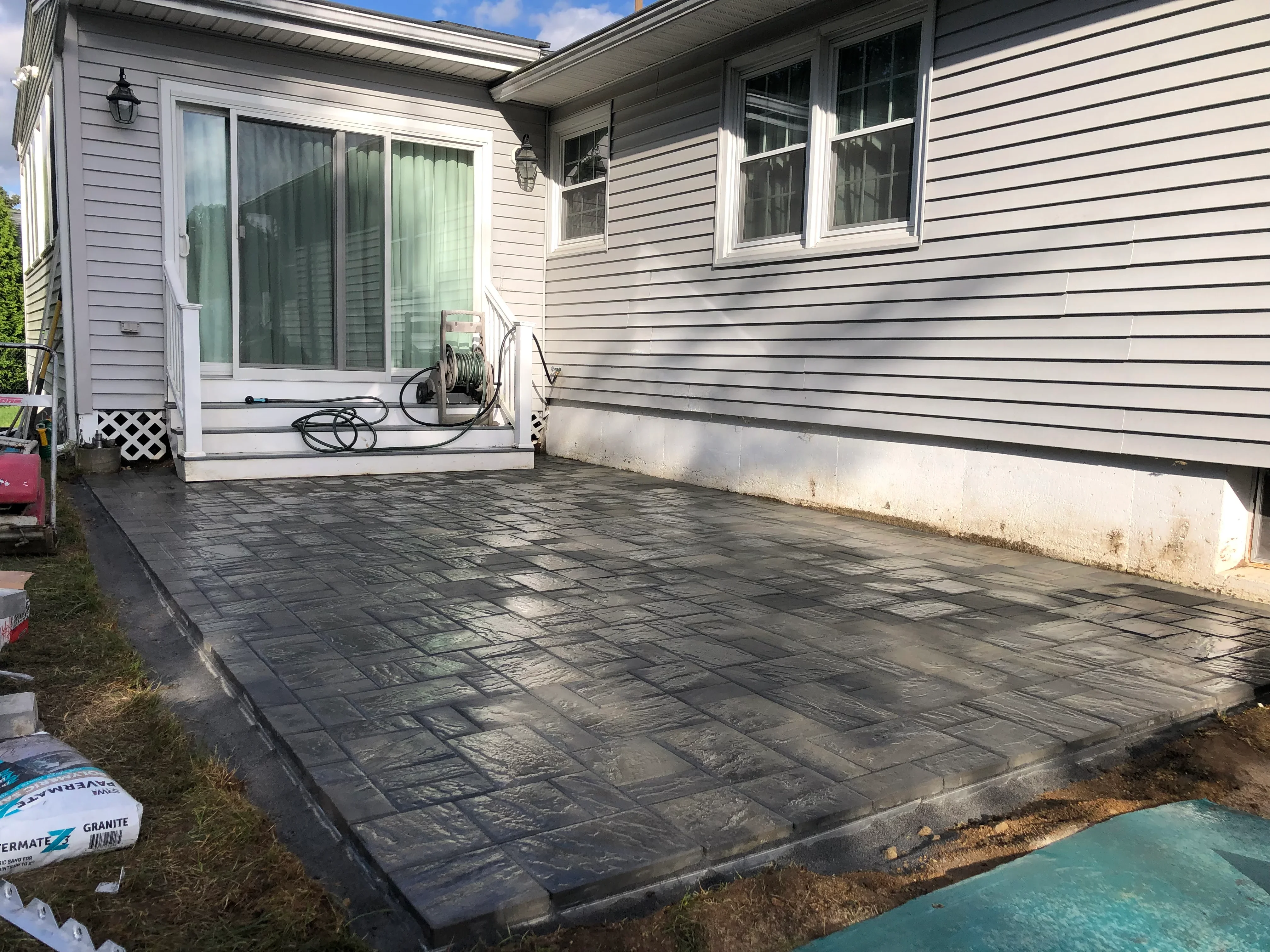 Charcoal gray paver patio with running bond pattern installed next to residential home
