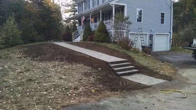 Sloped yard with fresh topsoil, concrete steps, and newly planted evergreen shrubs