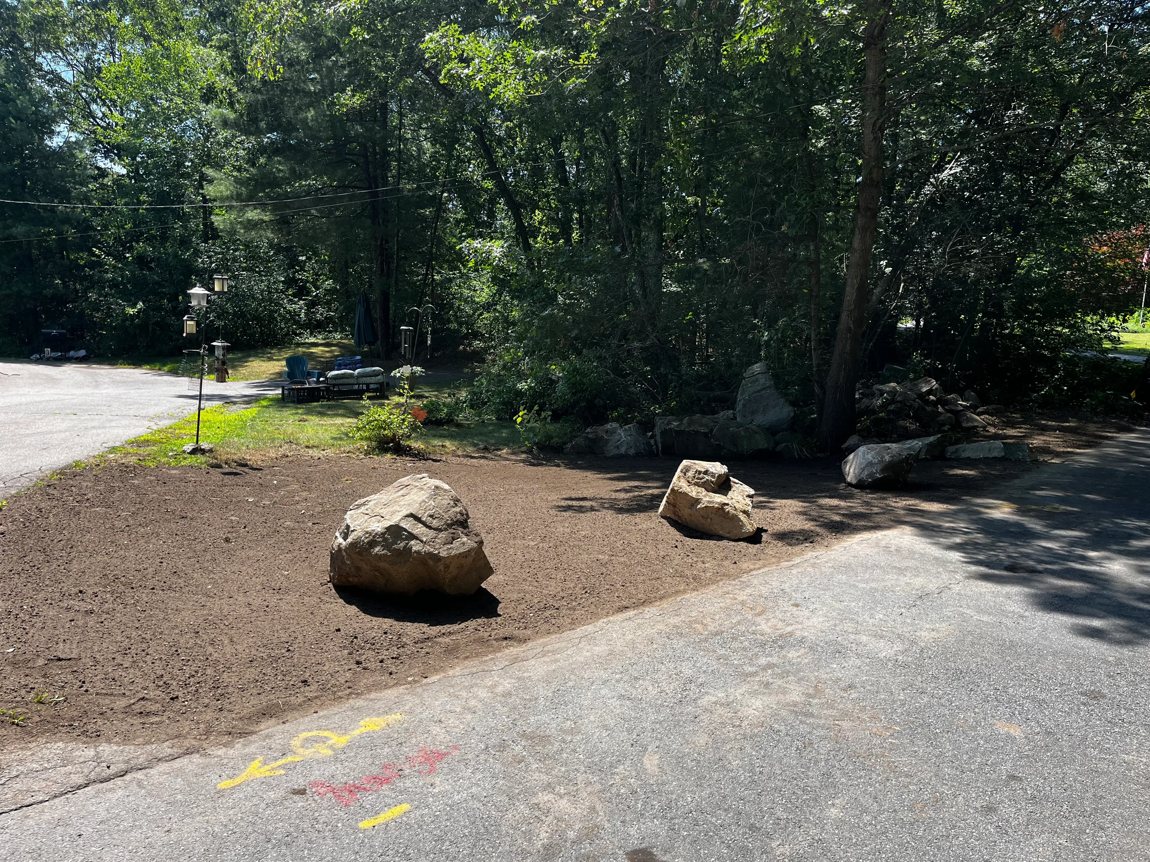 Mulched landscape bed with large boulders, mature trees, and natural woodland setting
