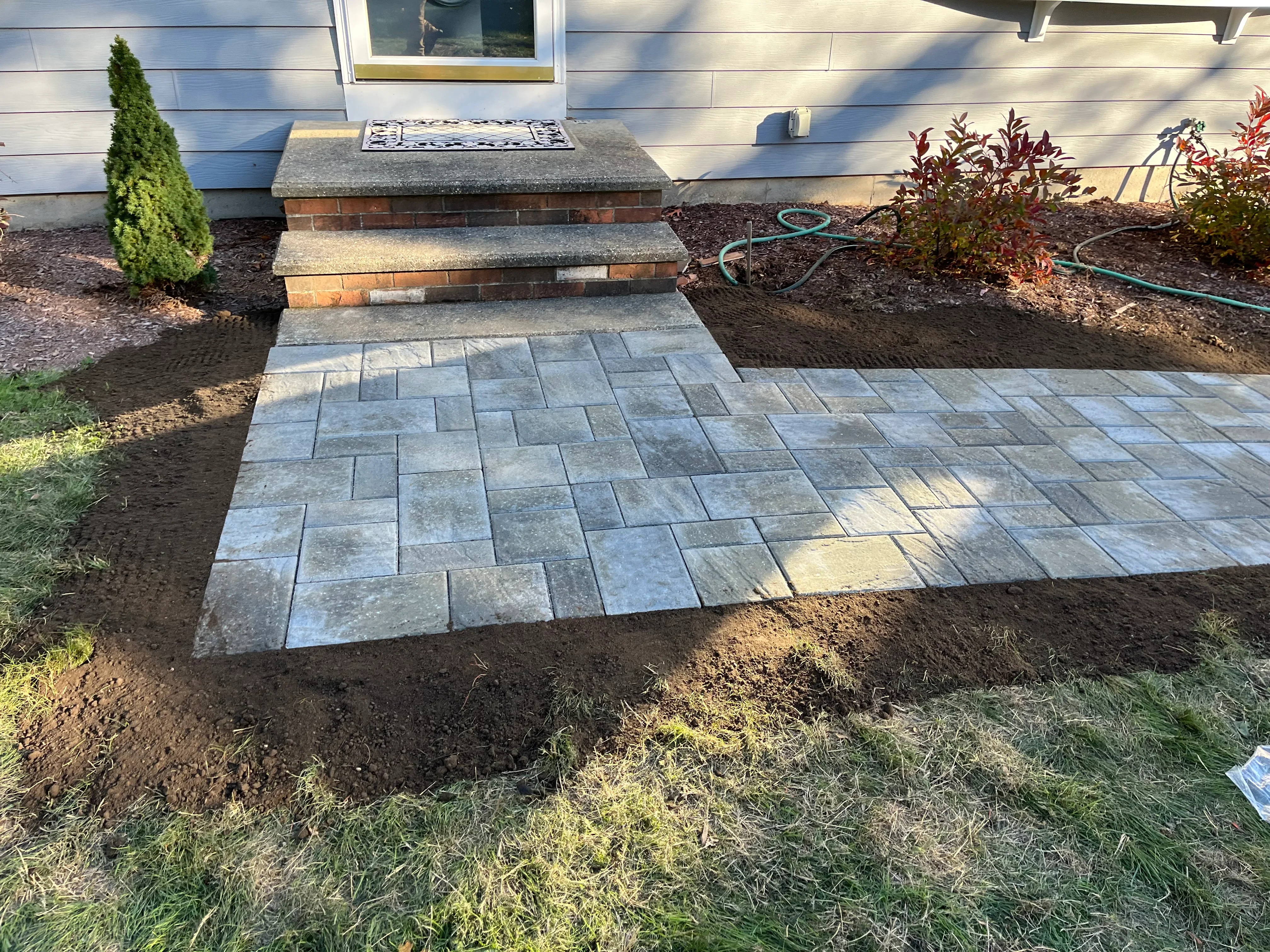 Gray concrete paver patio with running bond pattern, brick steps, and new mulch landscape beds