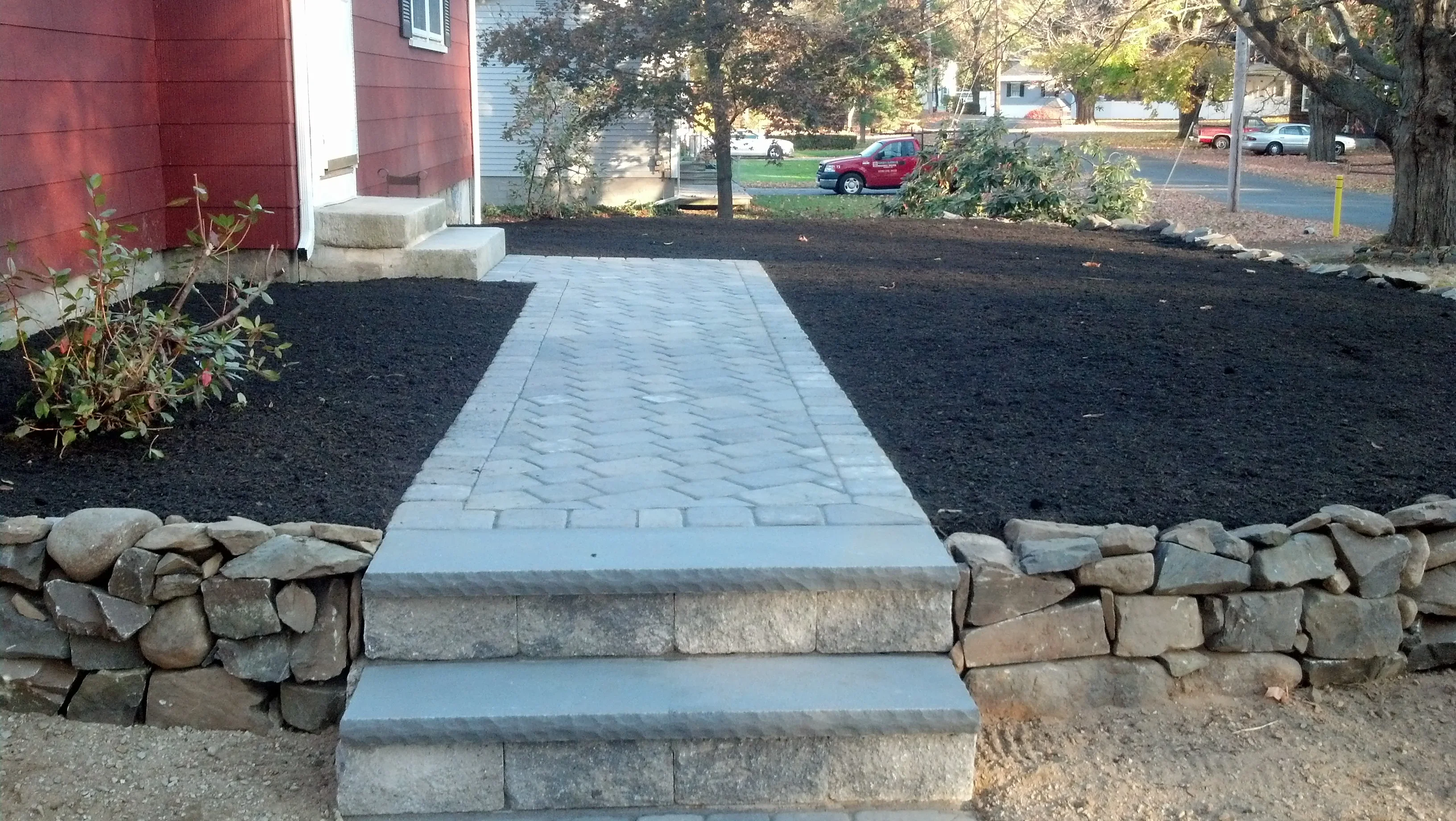 Gray paver walkway with herringbone pattern and stone retaining walls on both sides