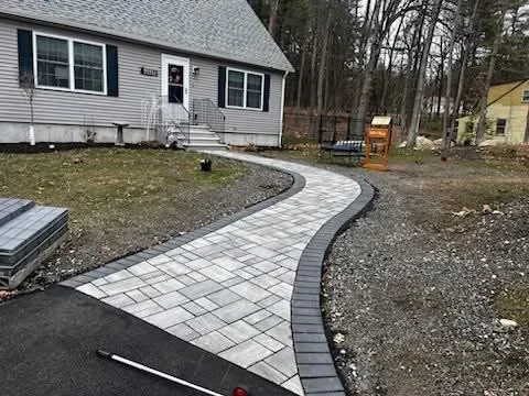 Curved paver walkway with gray pavers and dark border edging leading to home entrance