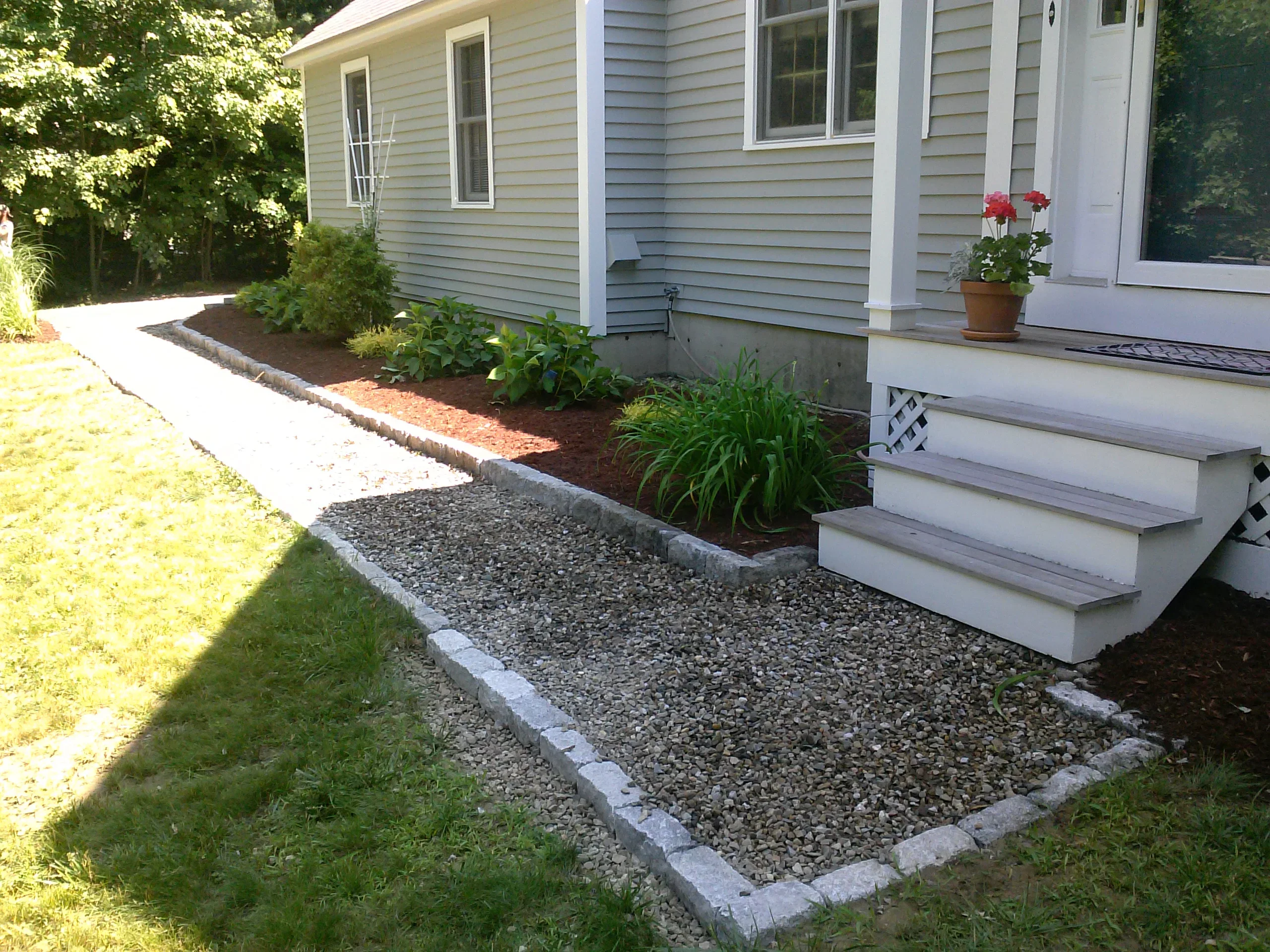 Concrete paver edging with gravel pathways, mulched planting beds, and ornamental shrubs along house foundation