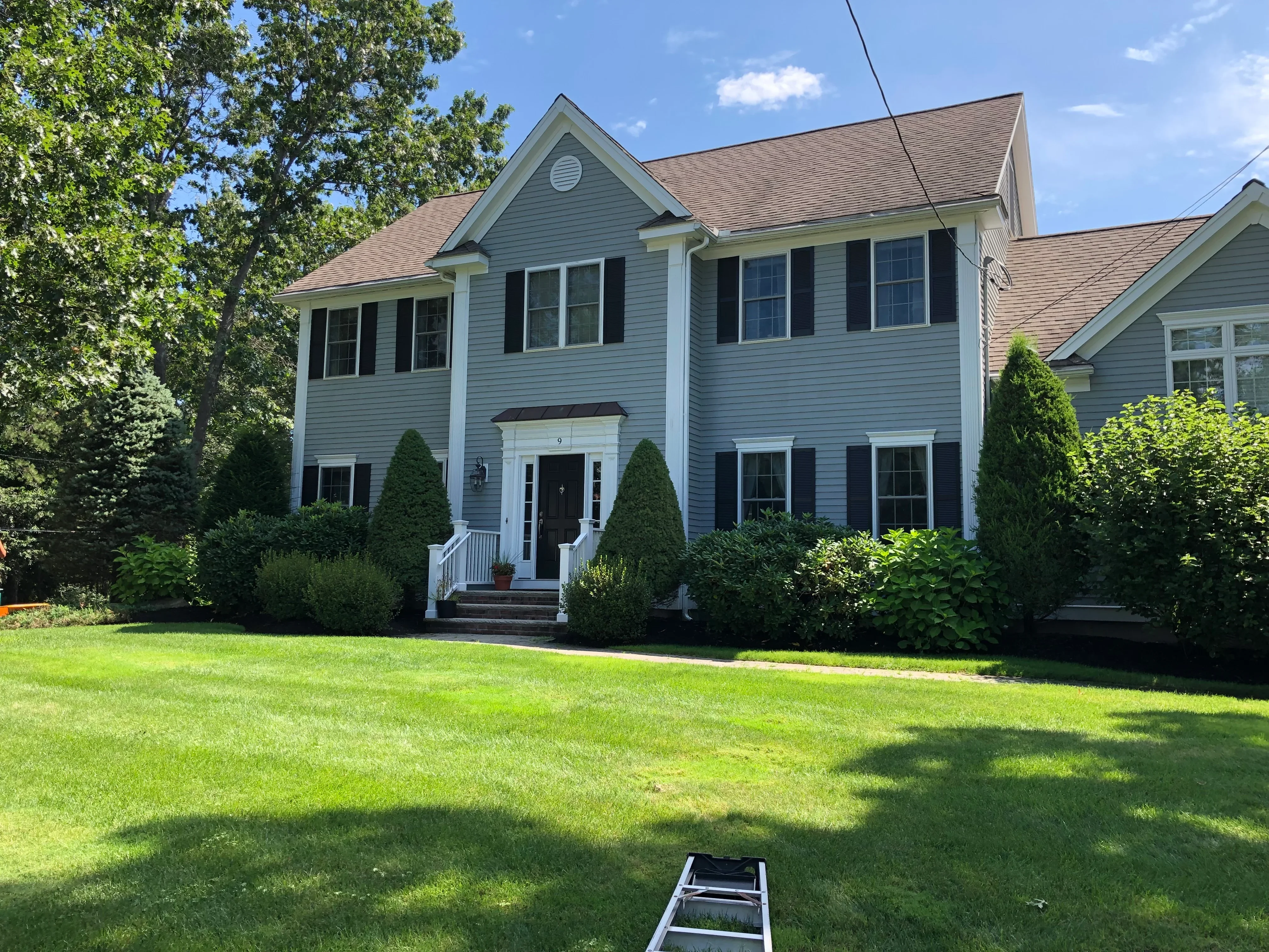 Two-story home with blue siding, white trim, and newly landscaped front yard with evergreen shrubs and lawn