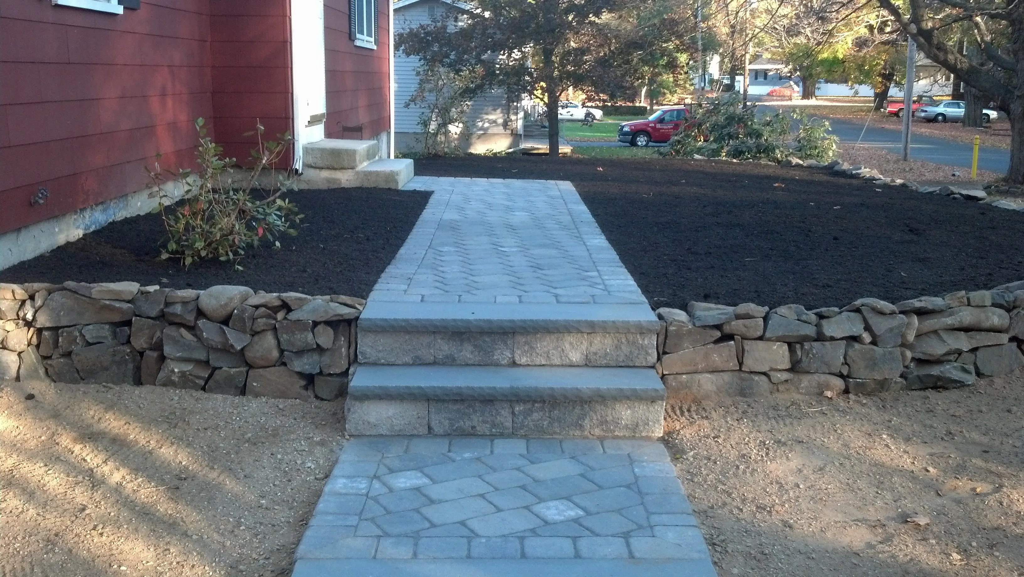 Light gray paver walkway with herringbone pattern and dry-stacked stone retaining wall