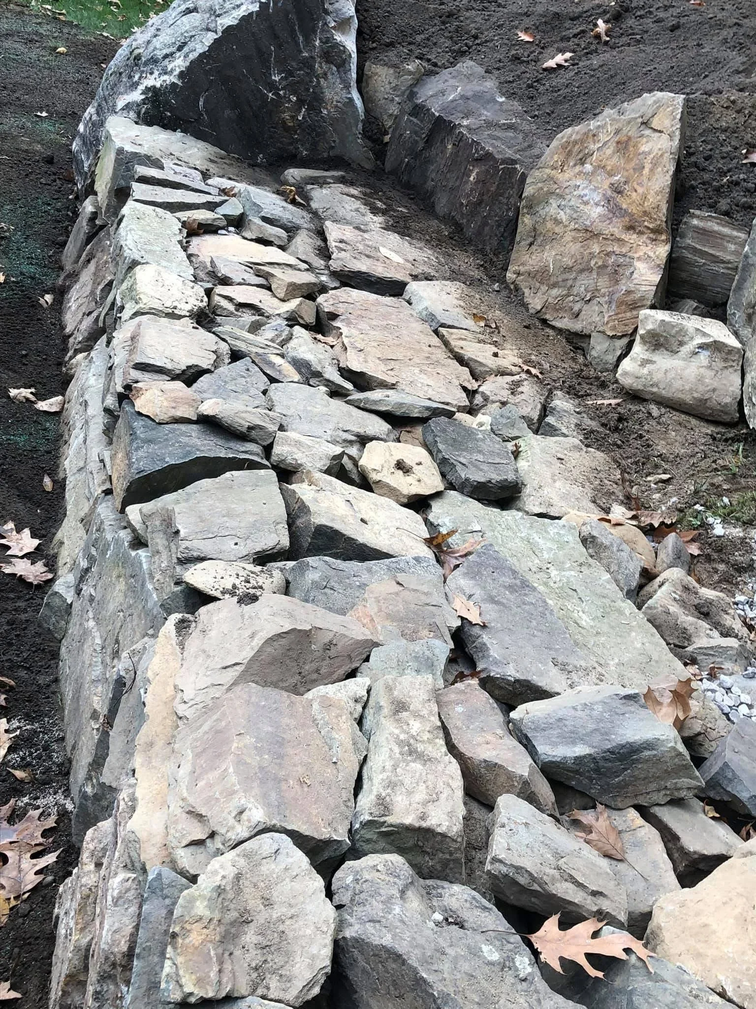 Dry stacked natural stone retaining wall with tan and gray flat stones, no mortar