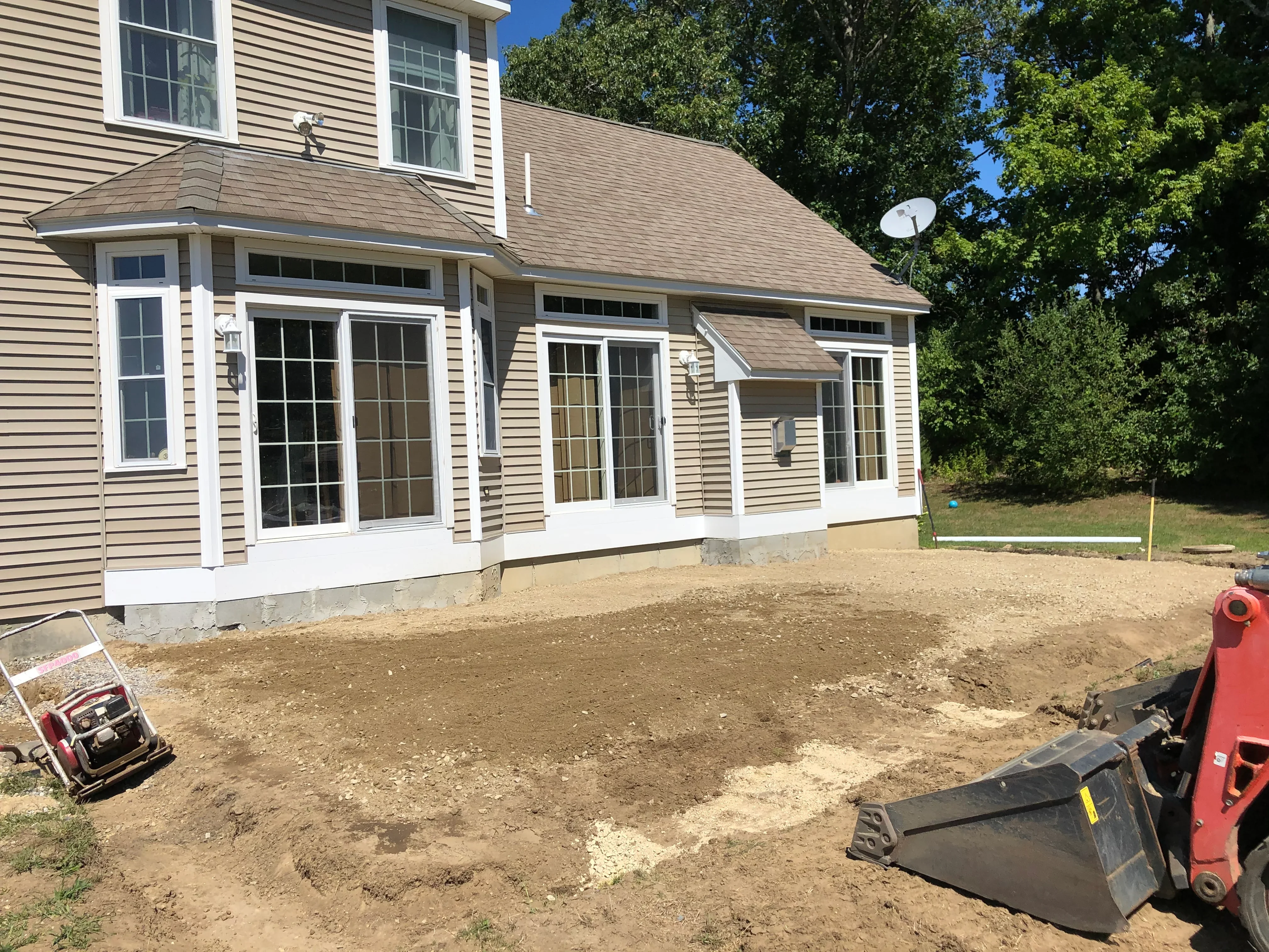 Graded dirt foundation area with heavy equipment beside new vinyl-sided home addition
