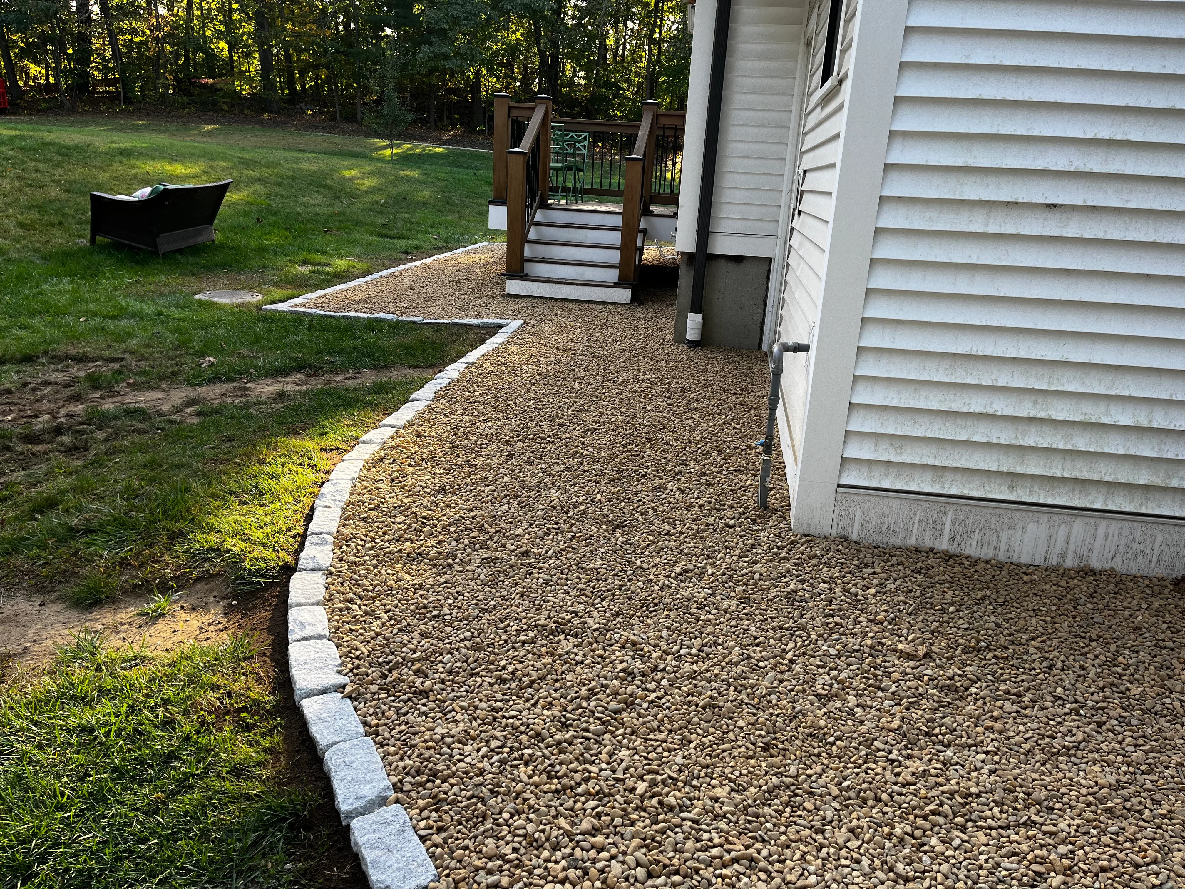 Tan gravel pathway with concrete paver edging leading to wooden deck with metal railing
