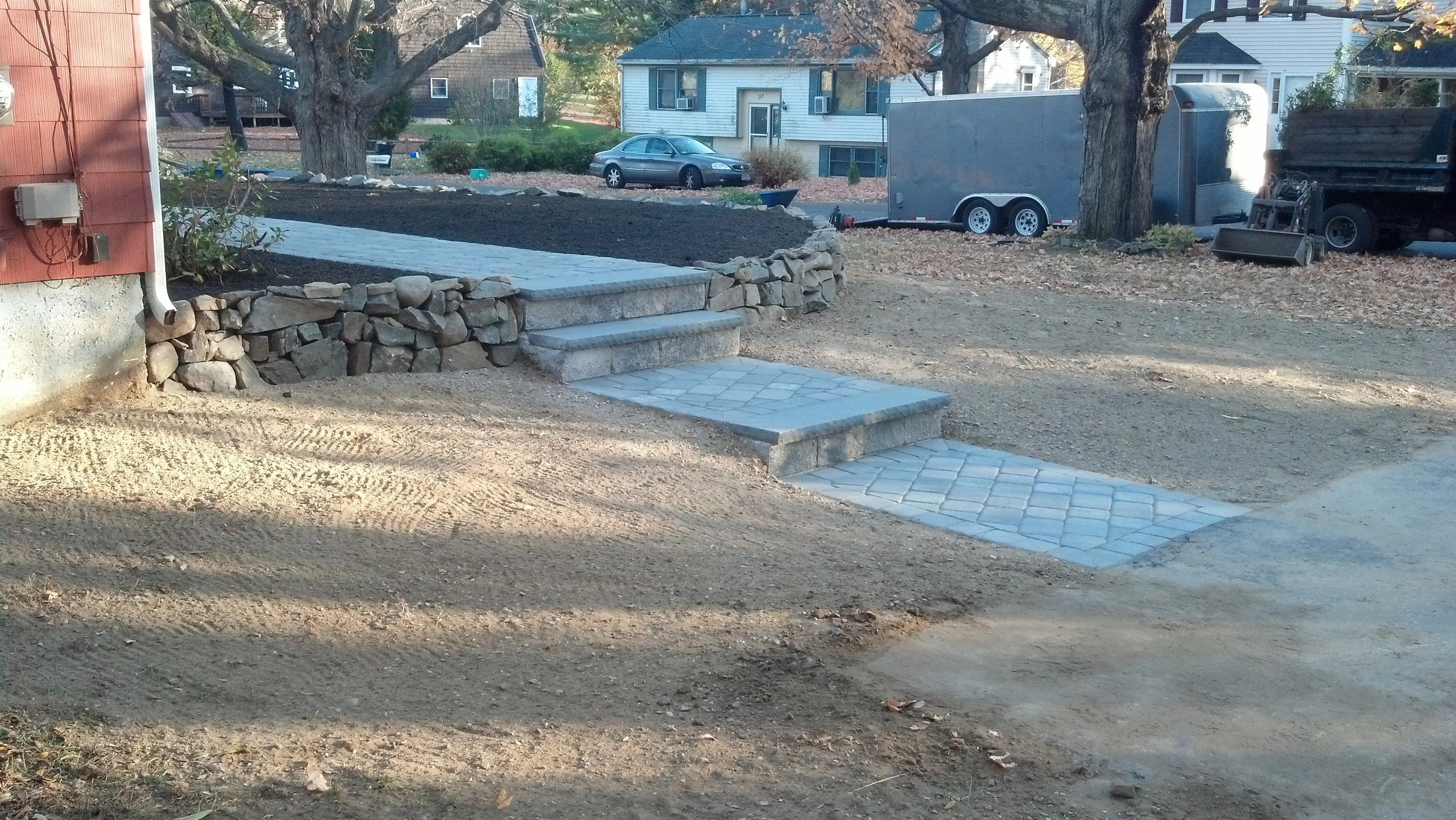 Stacked stone retaining wall with concrete steps and gray paver walkway on graded lot