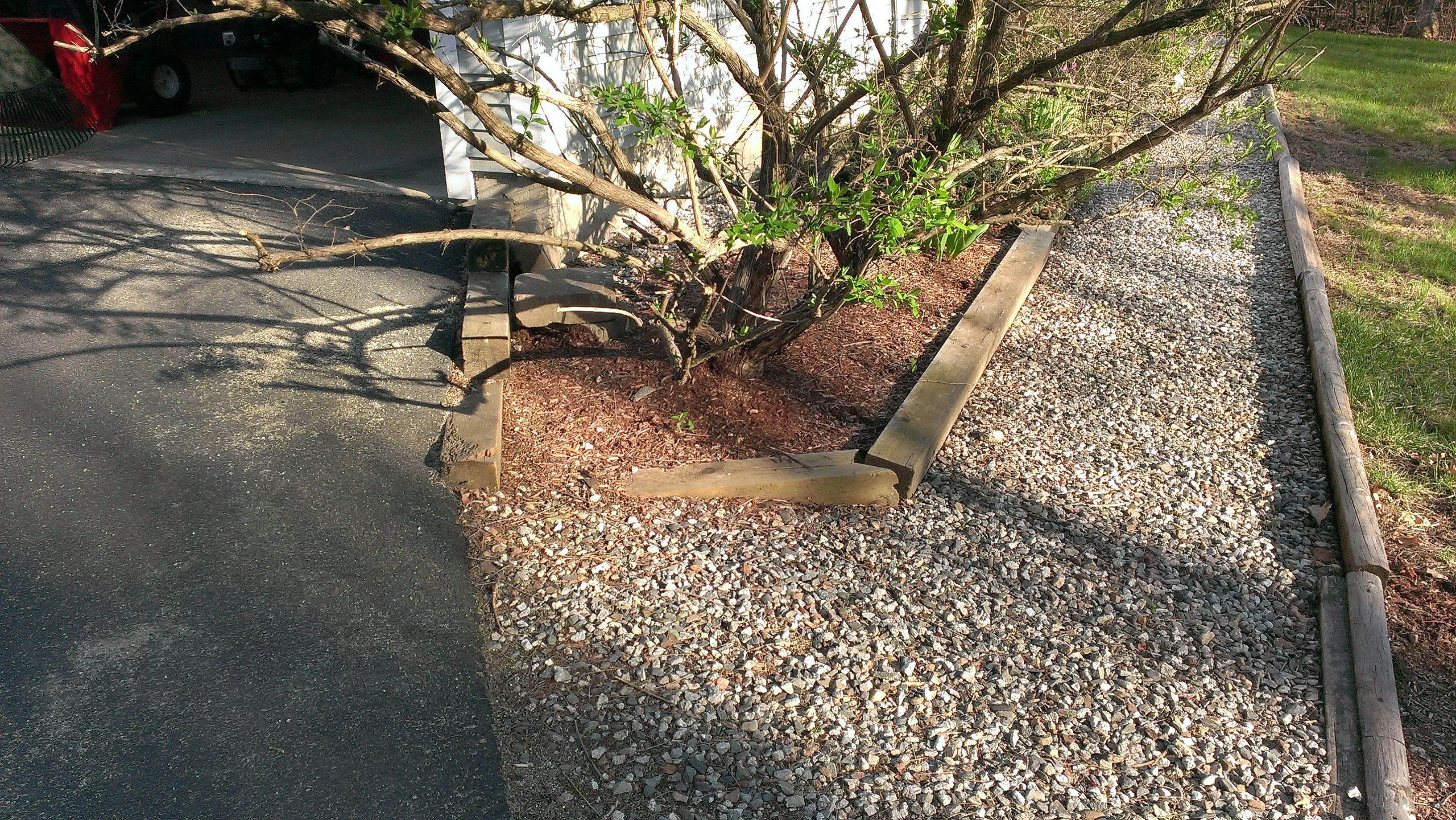 Gravel pathway with metal edging bordering asphalt and landscaped planting beds