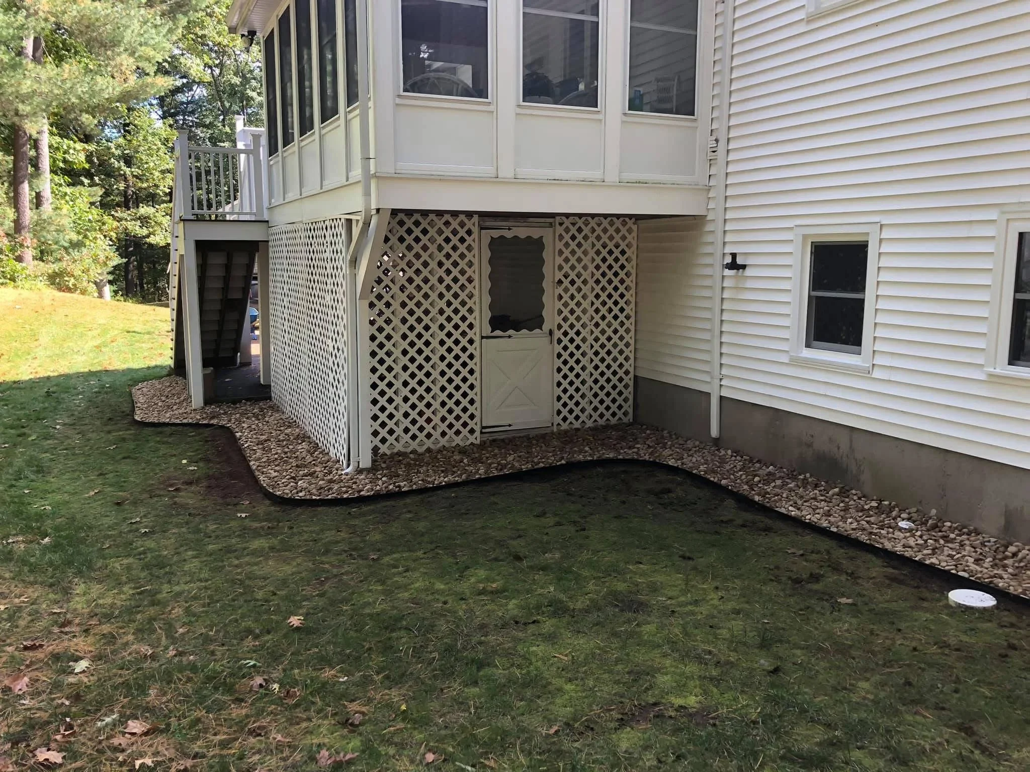 Under-deck drainage with white lattice skirting, gravel base, and landscape edging with river rock borders