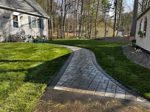 Curved dark gray paver walkway with light border pavers through residential yard with lawn and trees