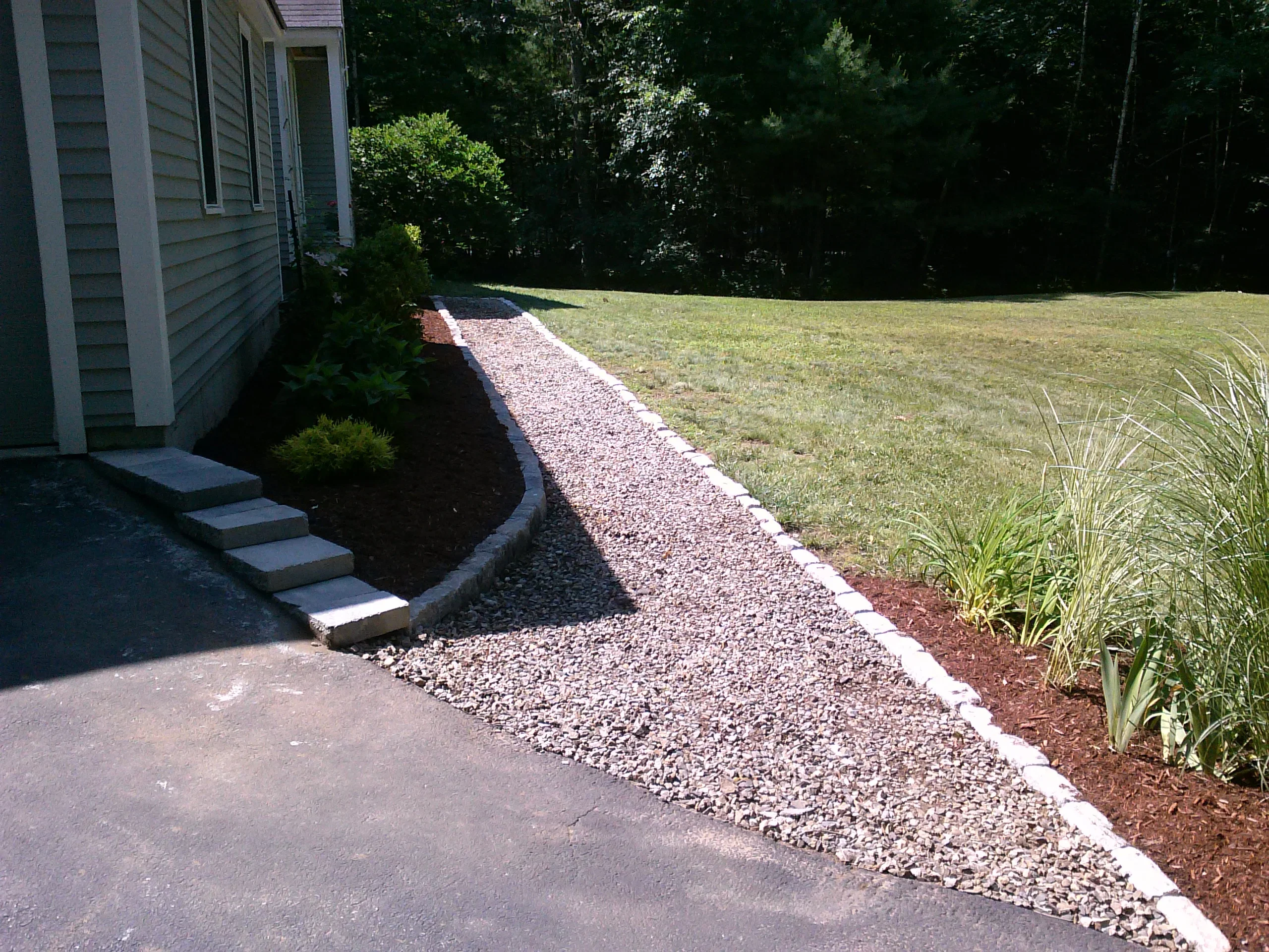 Gravel pathway with white edging, dark mulch beds, and ornamental plants along house foundation