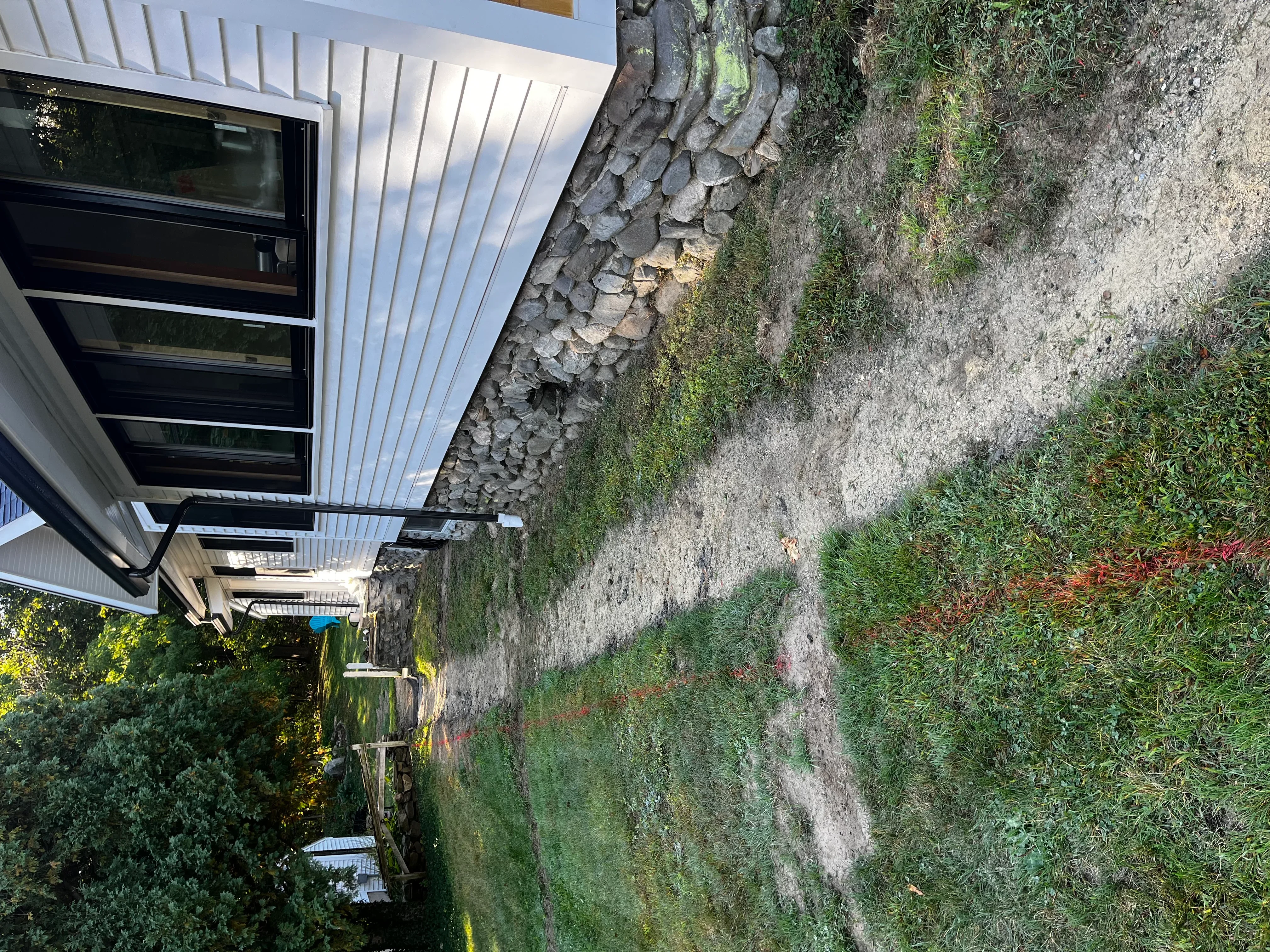 Stacked stone retaining wall with landscape plantings and modern residential structure