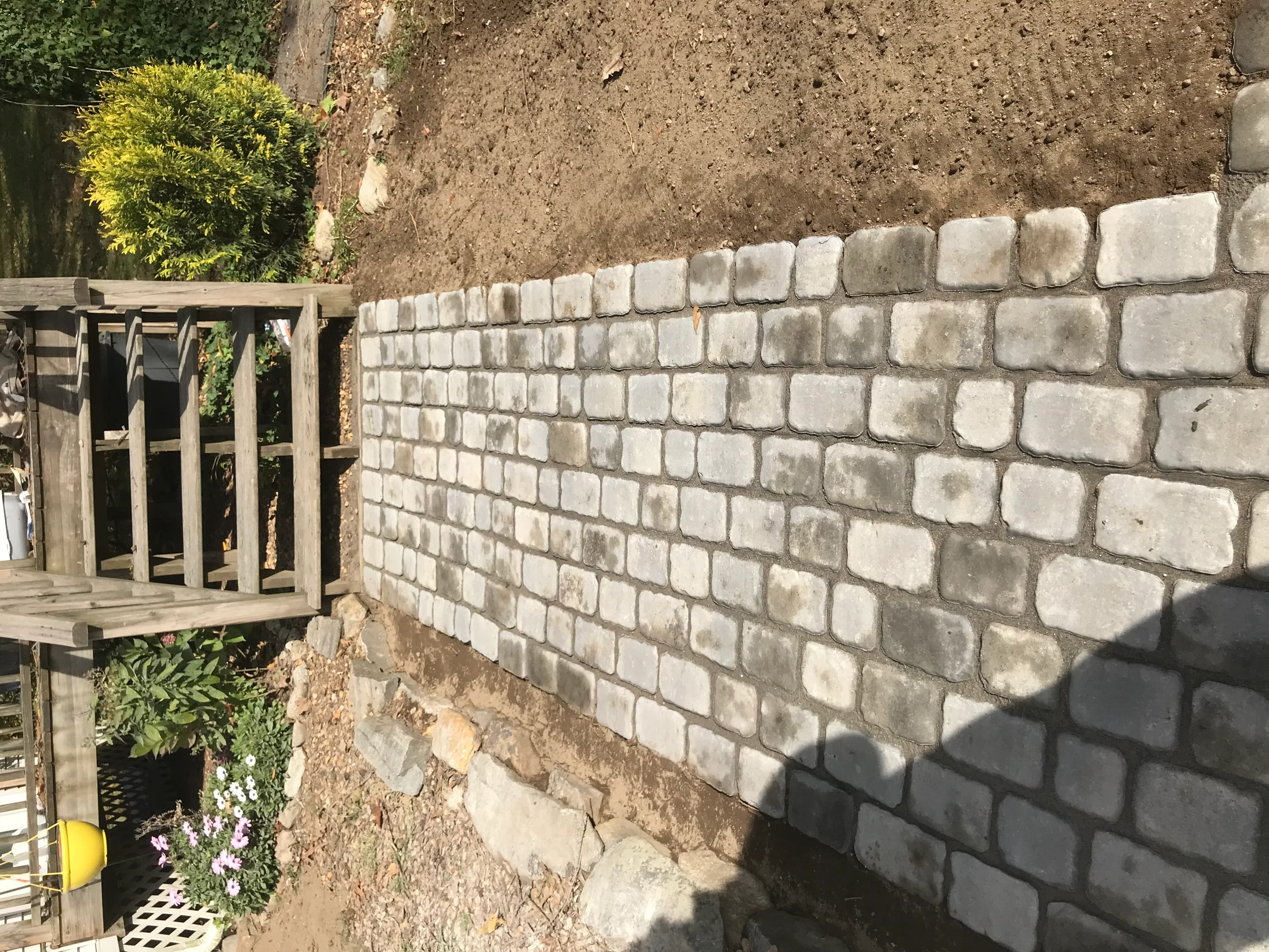 Concrete block retaining wall with gray blocks in running bond pattern and compacted soil backfill