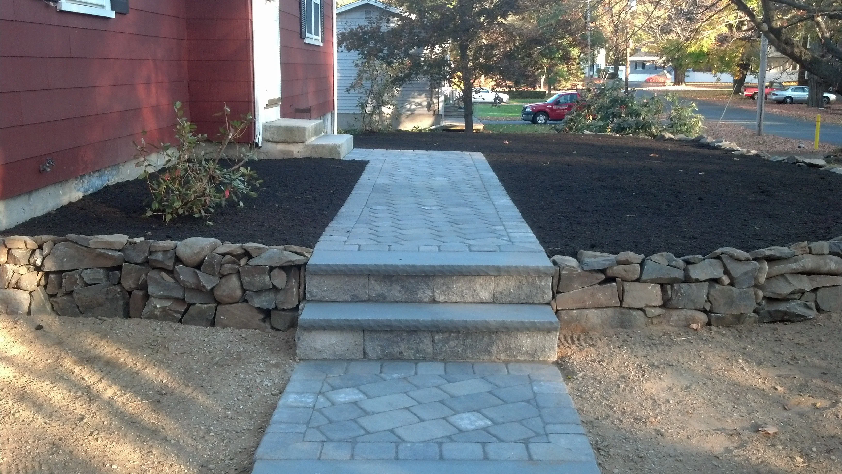 Gray paver walkway with geometric pattern and dry-stacked stone retaining wall in front yard