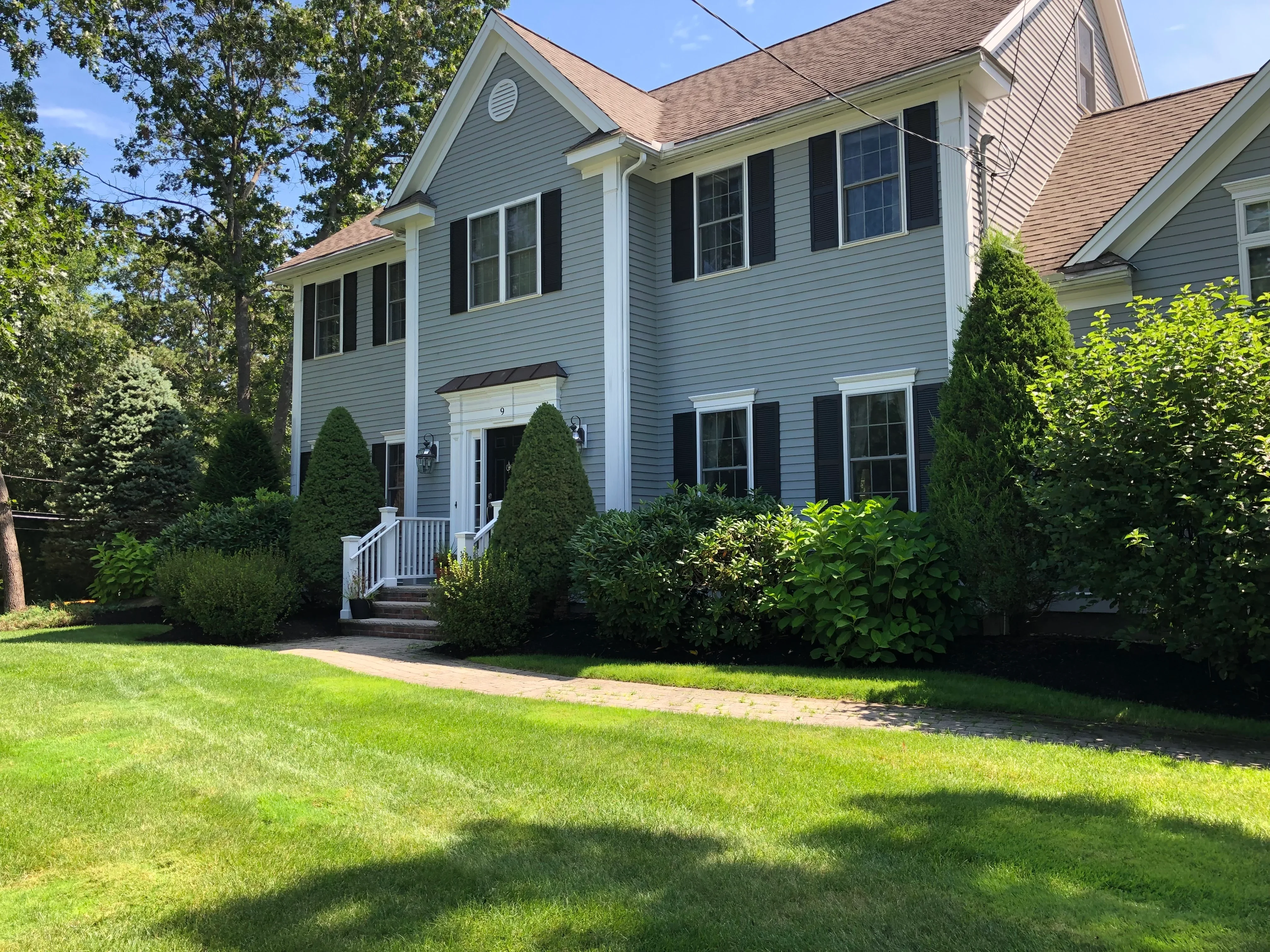 Light blue two-story home with layered foundation plantings including evergreen shrubs and ornamental grasses