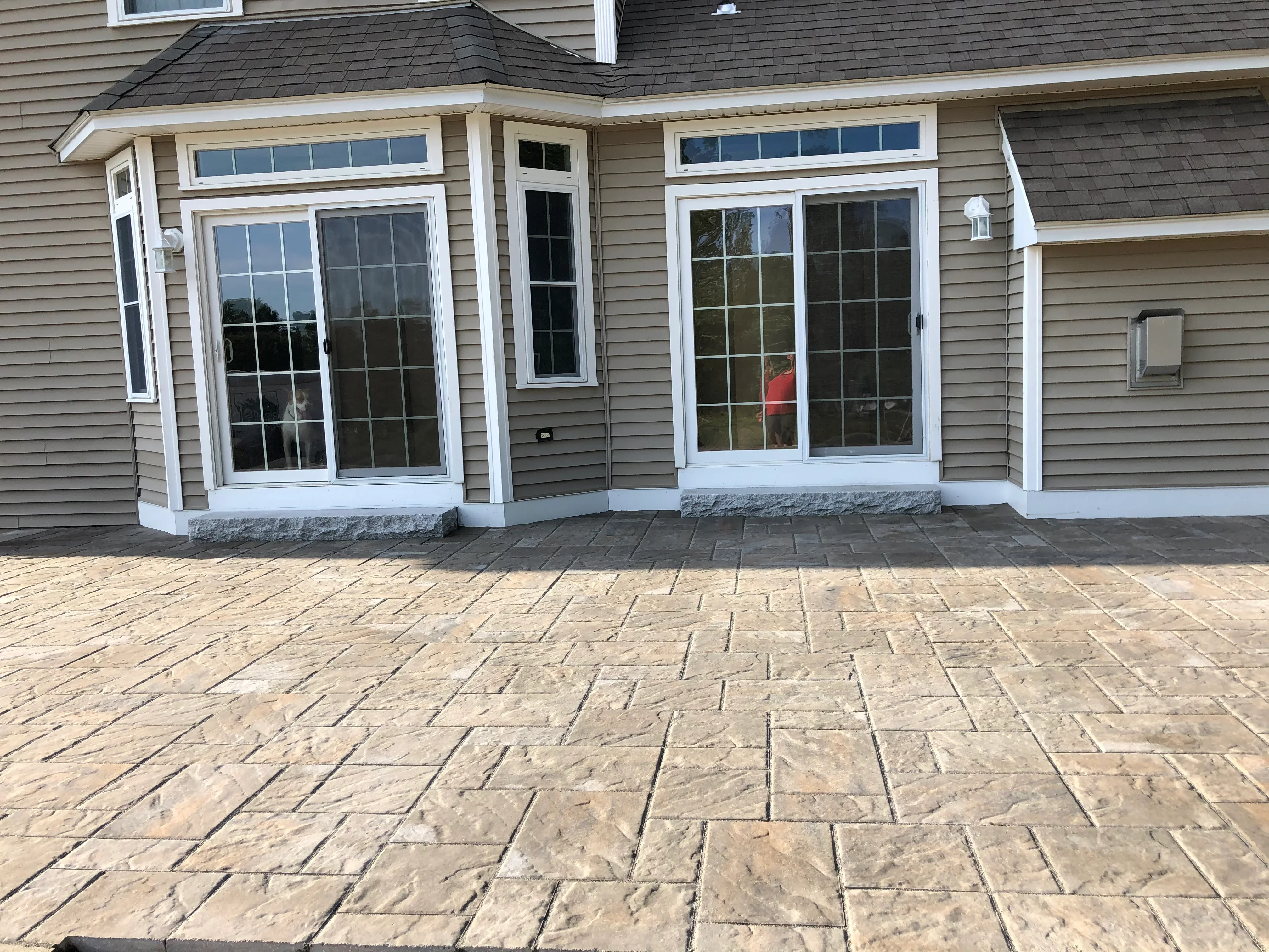 Stamped concrete patio with ashlar slate pattern in front of residential home with white-trimmed glass doors