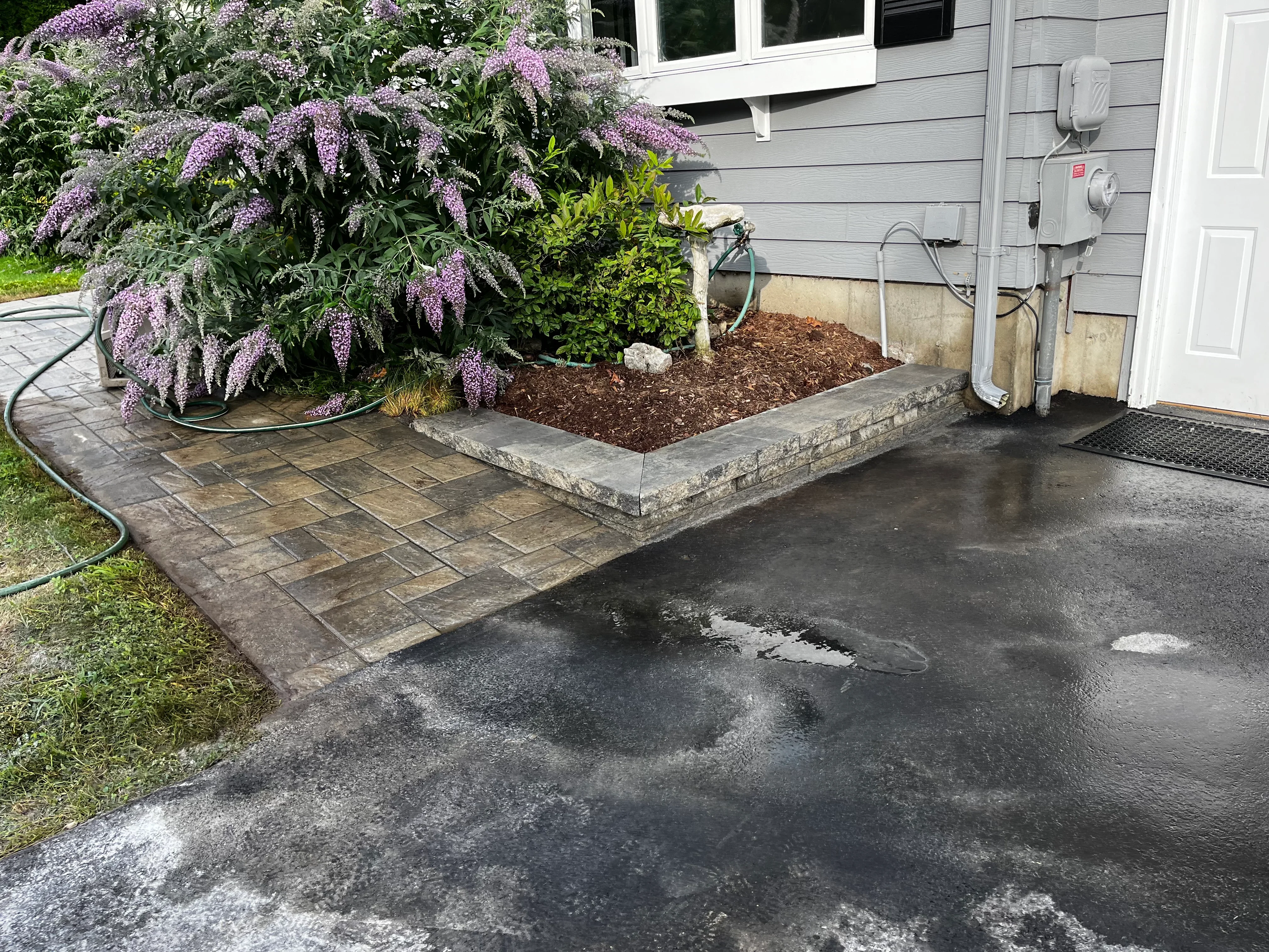 Stamped concrete patio with geometric paver pattern and raised stone planting bed with purple flowering shrubs