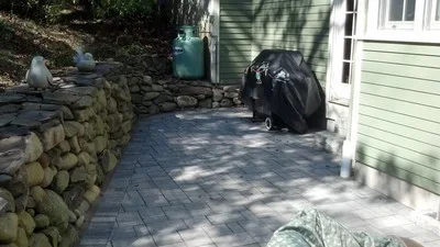 Dark gray paver patio with stacked stone retaining wall in residential yard