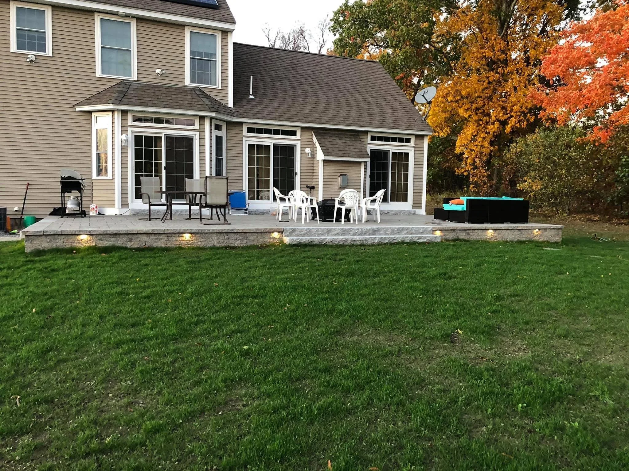 Stone paver patio with integrated lighting, French doors, and manicured lawn