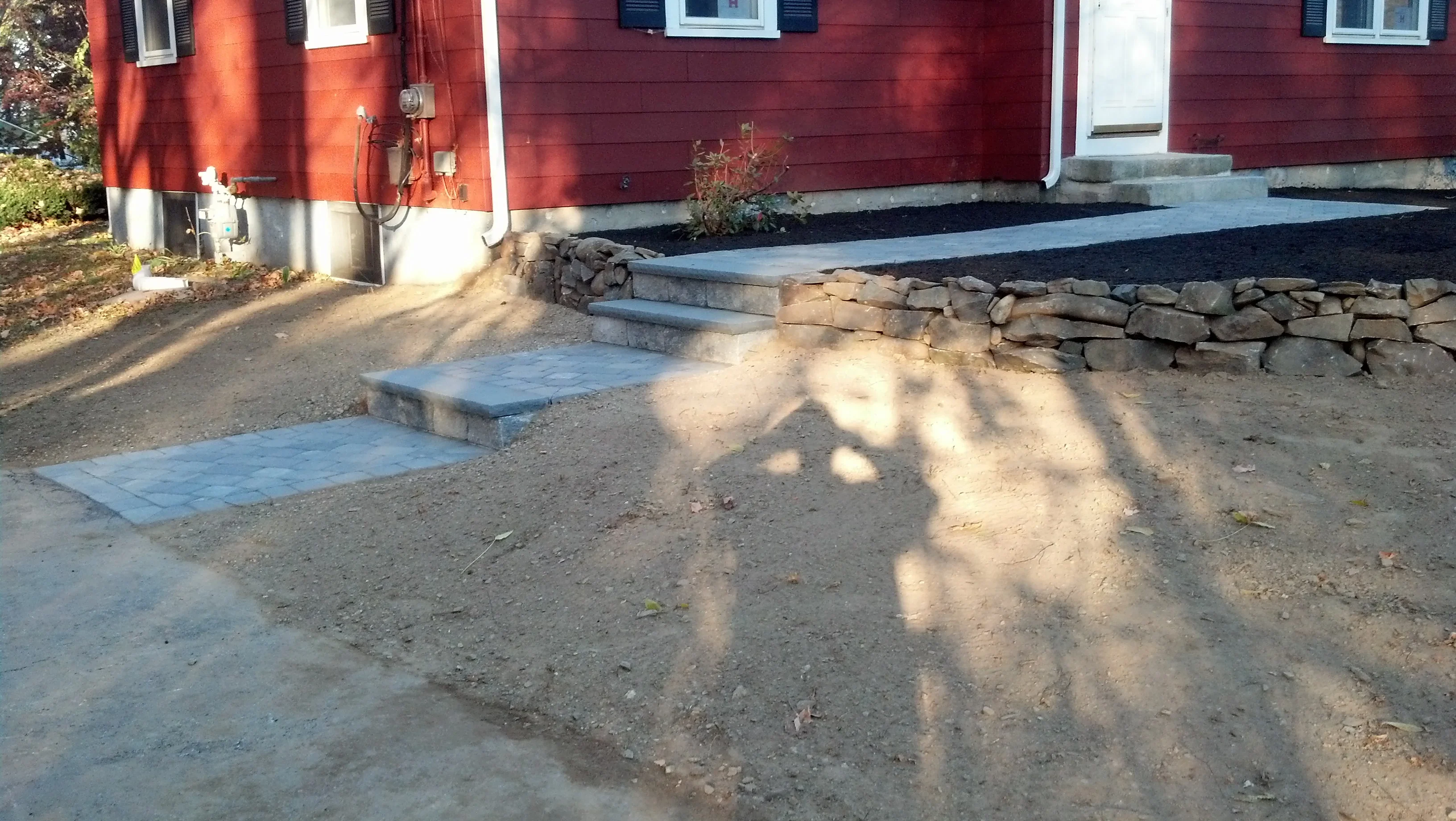 Concrete paver walkway with dry-stacked stone retaining wall and graded landscape bed