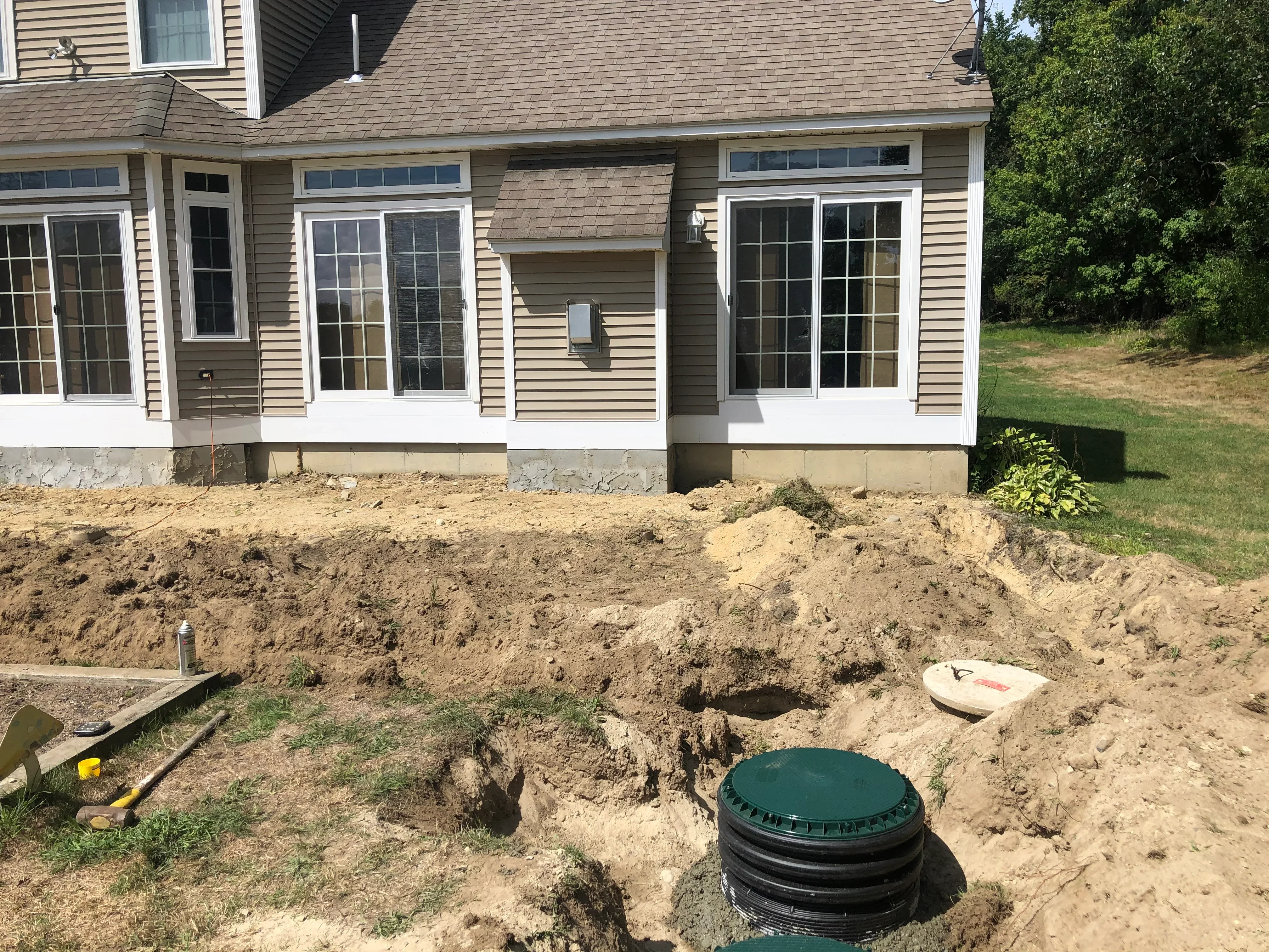 Septic tank installation with excavated soil and green tank cover in front of residential home
