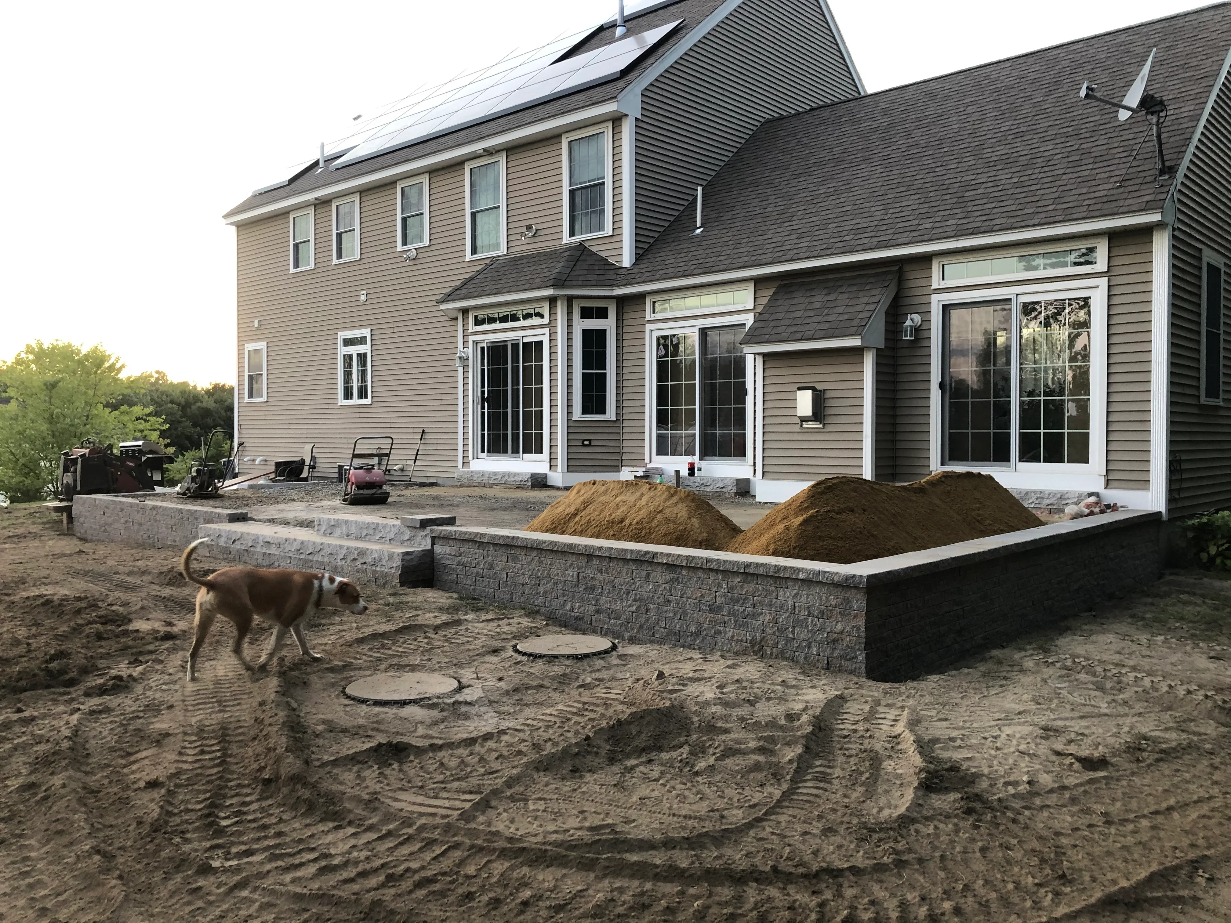 Stacked stone retaining walls with graded soil and landscape materials during construction phase