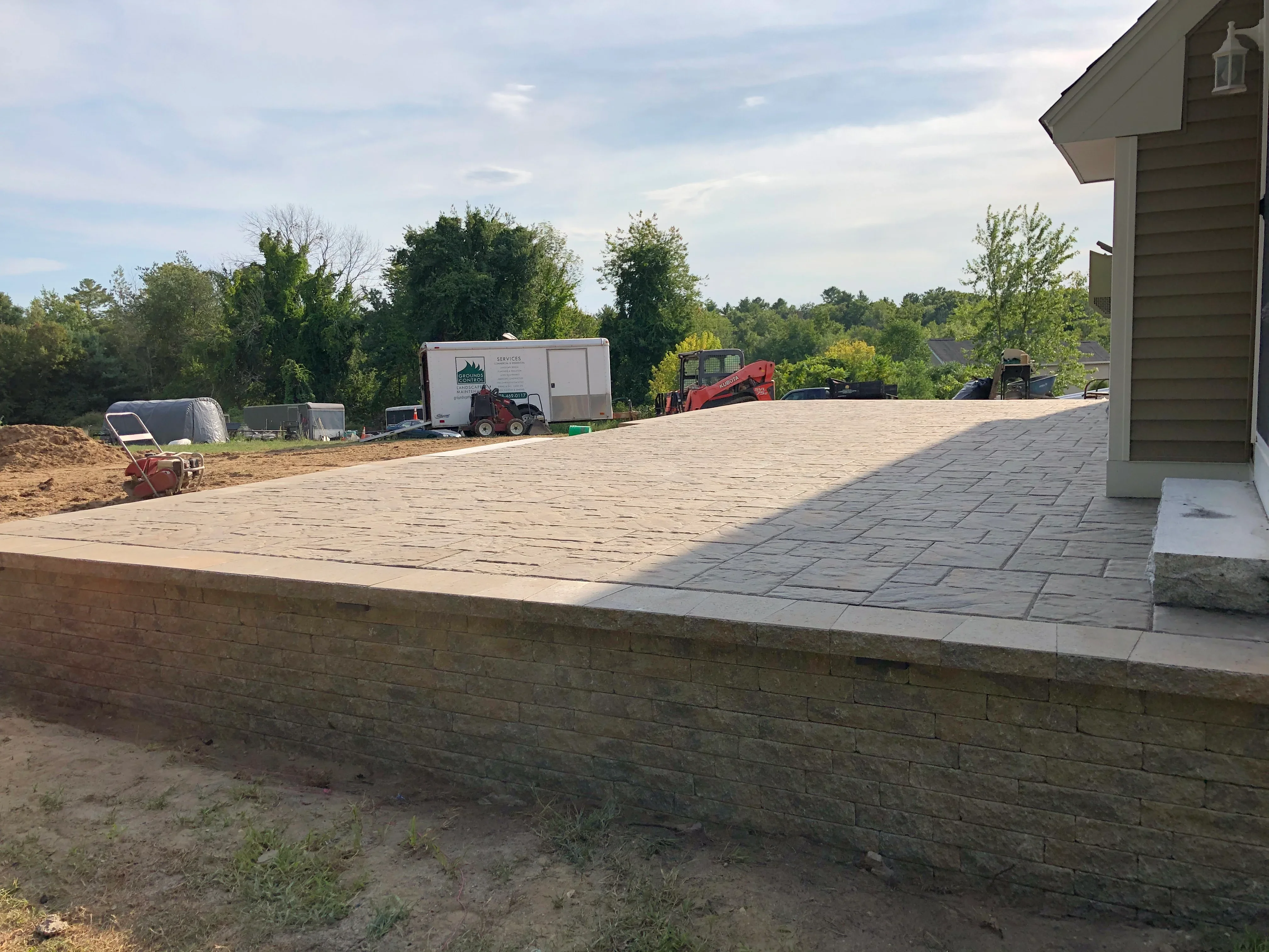 Tumbled brick paver patio with stone retaining wall during installation