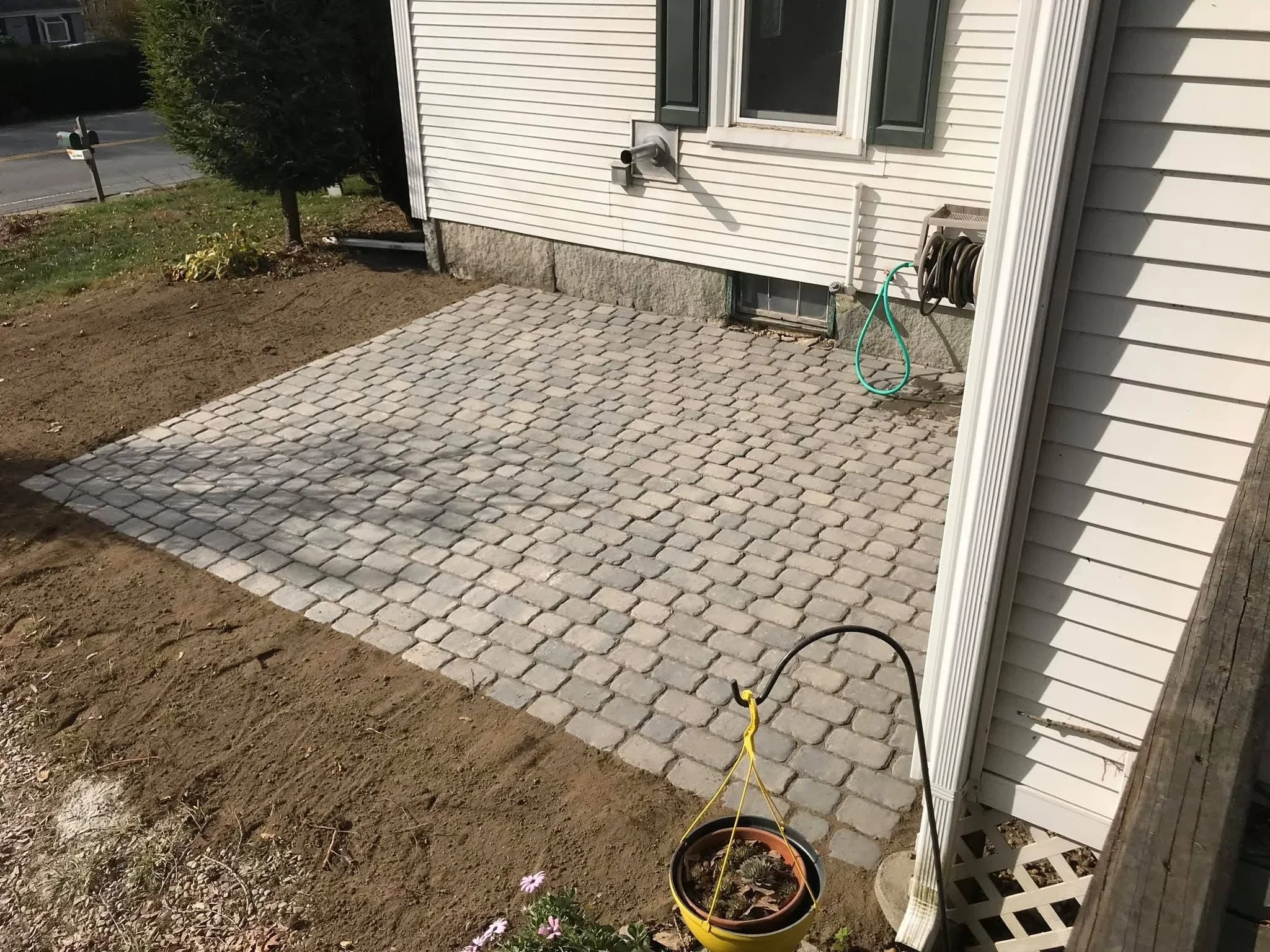 Gray permeable brick paver patio installed next to house foundation with white vinyl siding