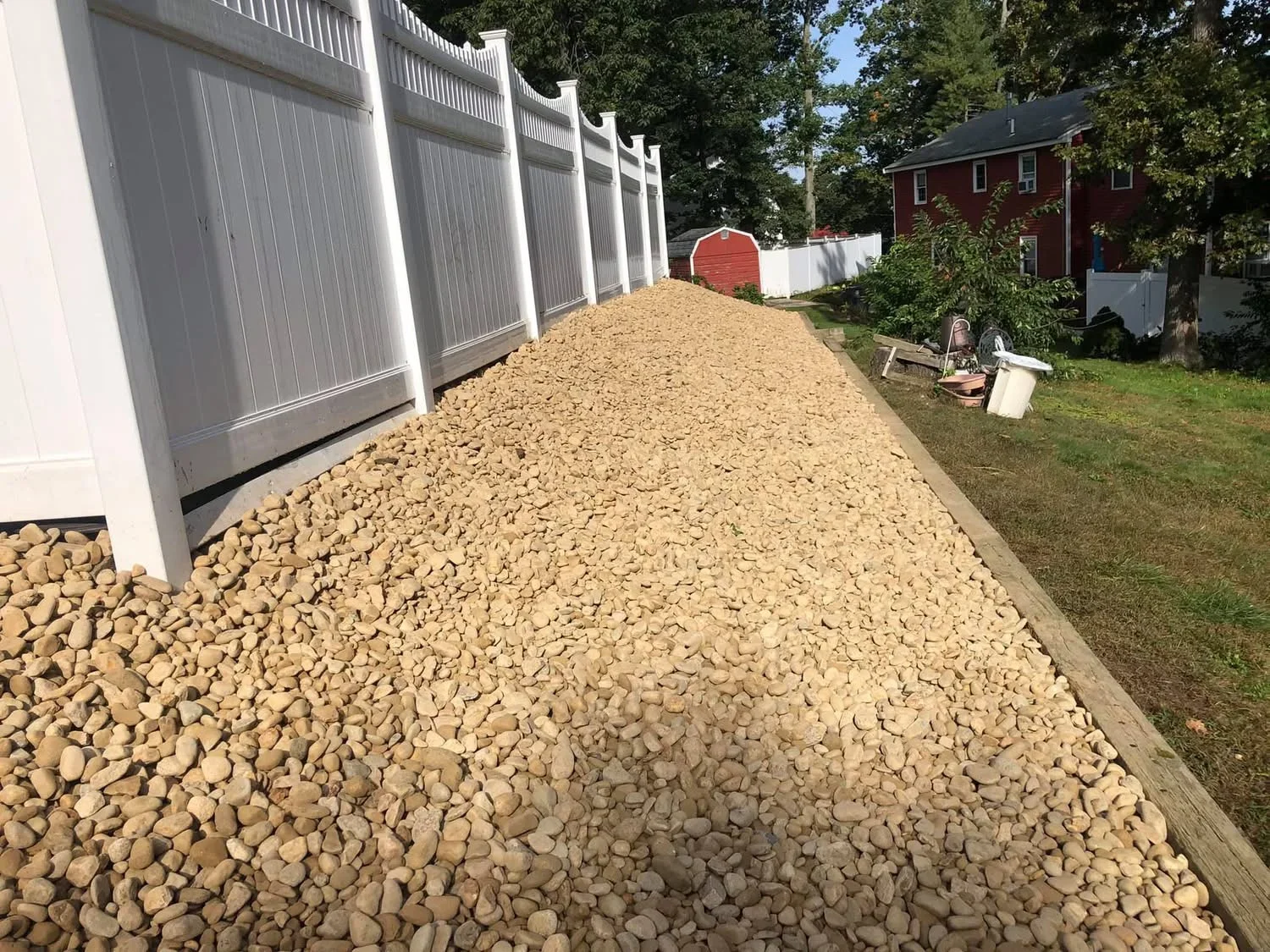 Tan pea gravel pathway with metal edging alongside white vinyl fence and residential building