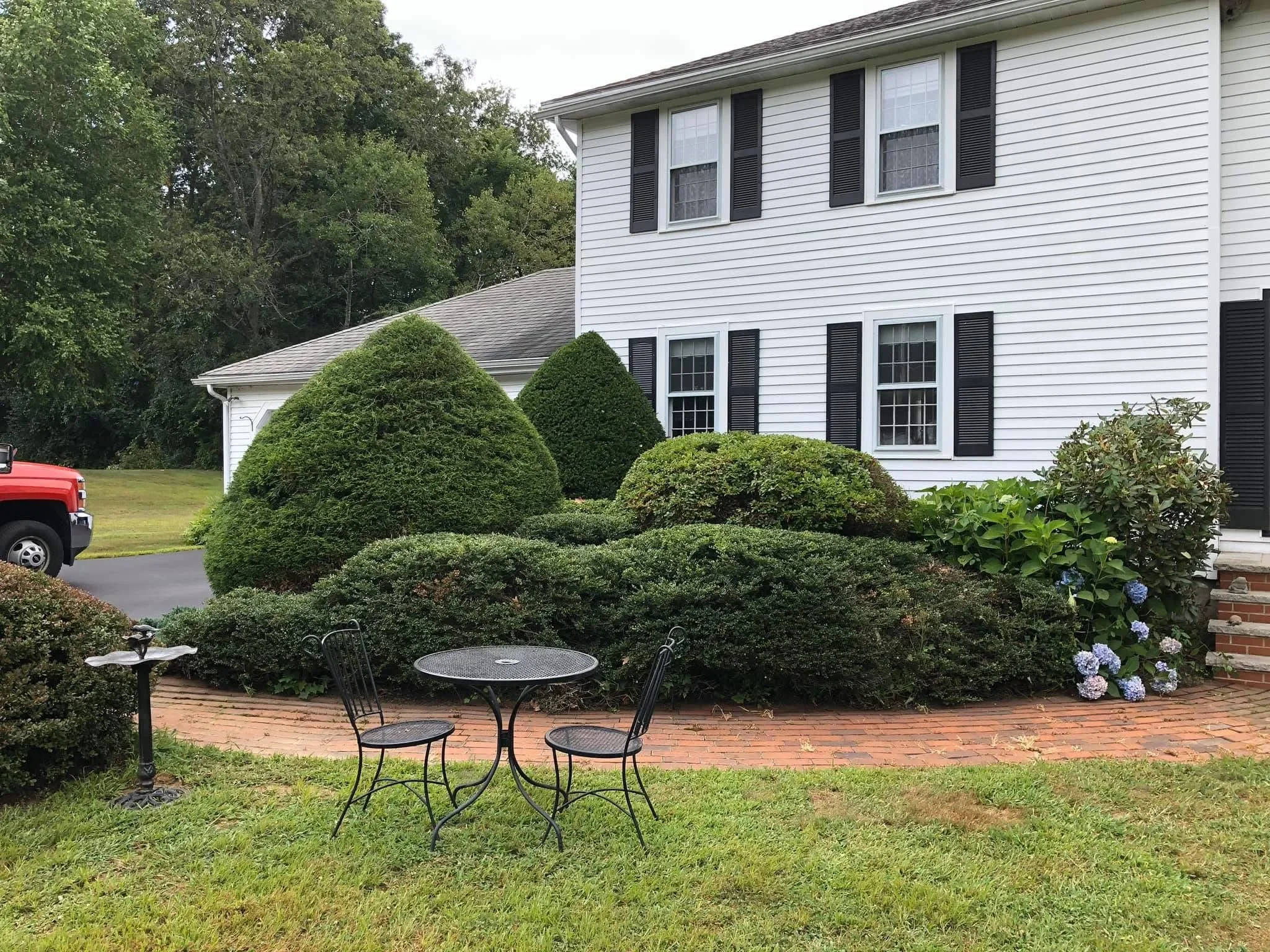 Shaped boxwood topiaries, foundation plantings, brick patio with seating, and hydrangea flowers