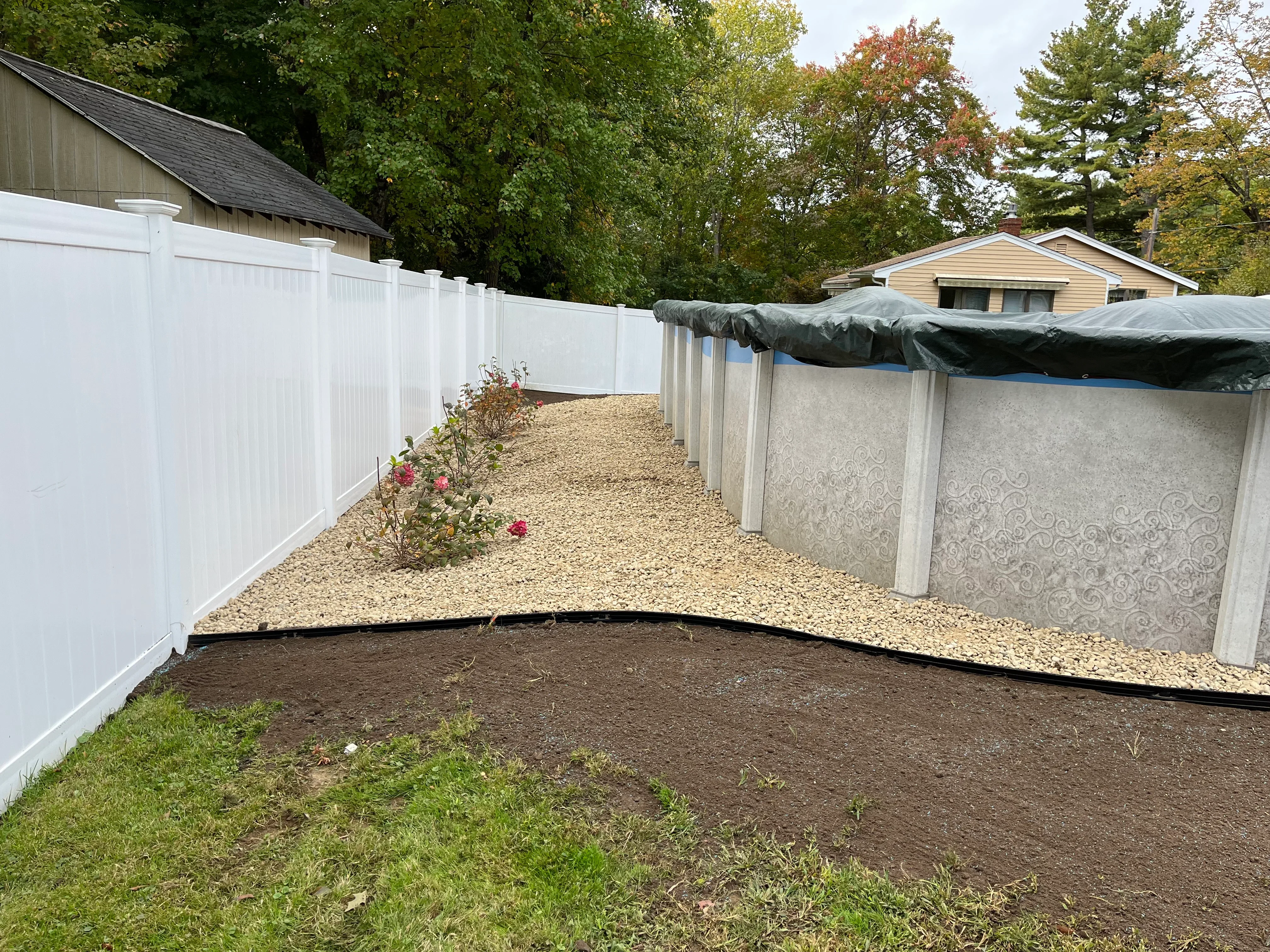 White vinyl fence, gravel base, landscape edging, and prepared soil in residential backyard