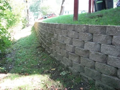 Stacked concrete block retaining wall on sloped residential property with lawn above