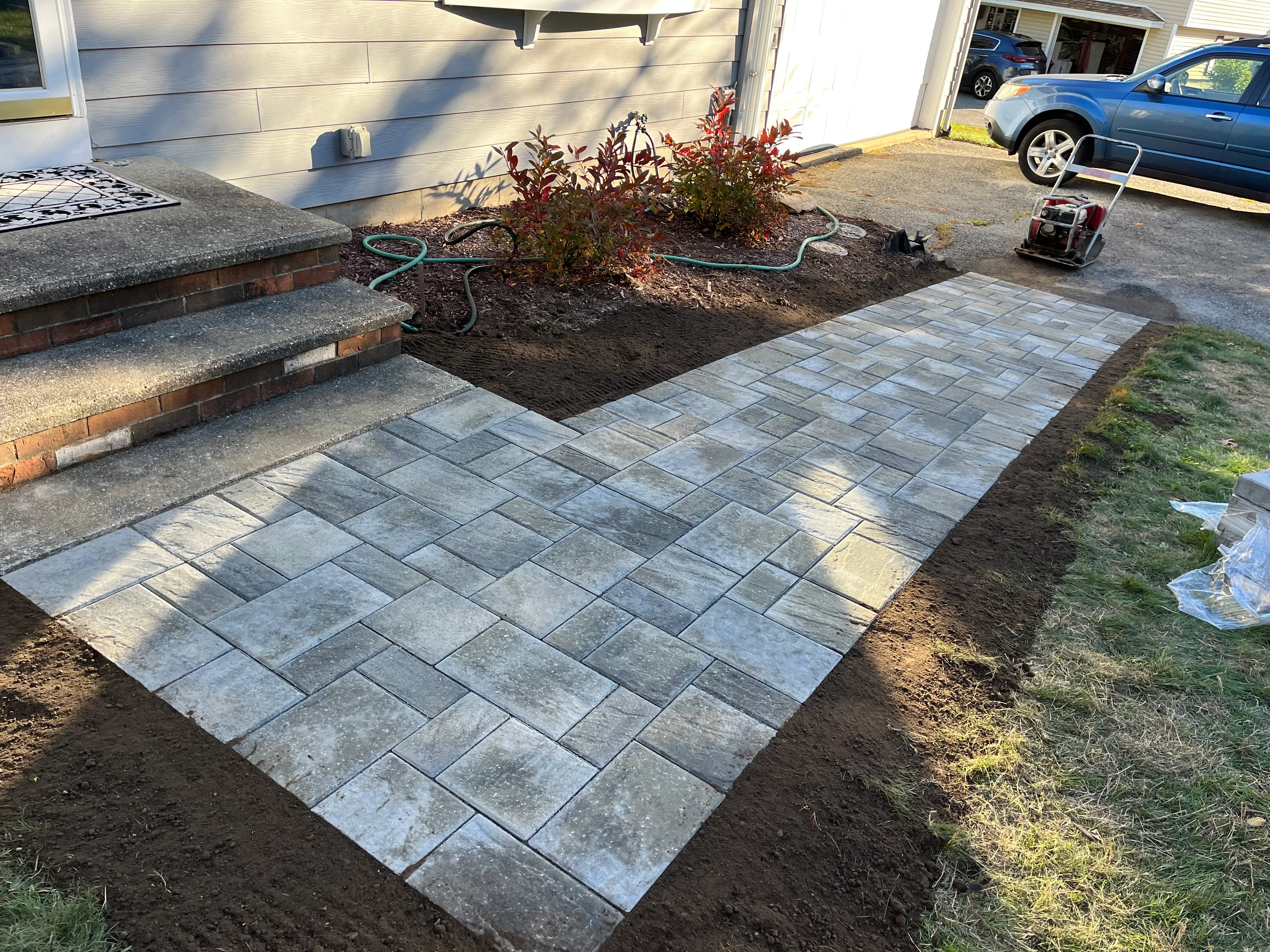 Gray concrete pavers in herringbone pattern with mulched planting bed and ornamental shrubs