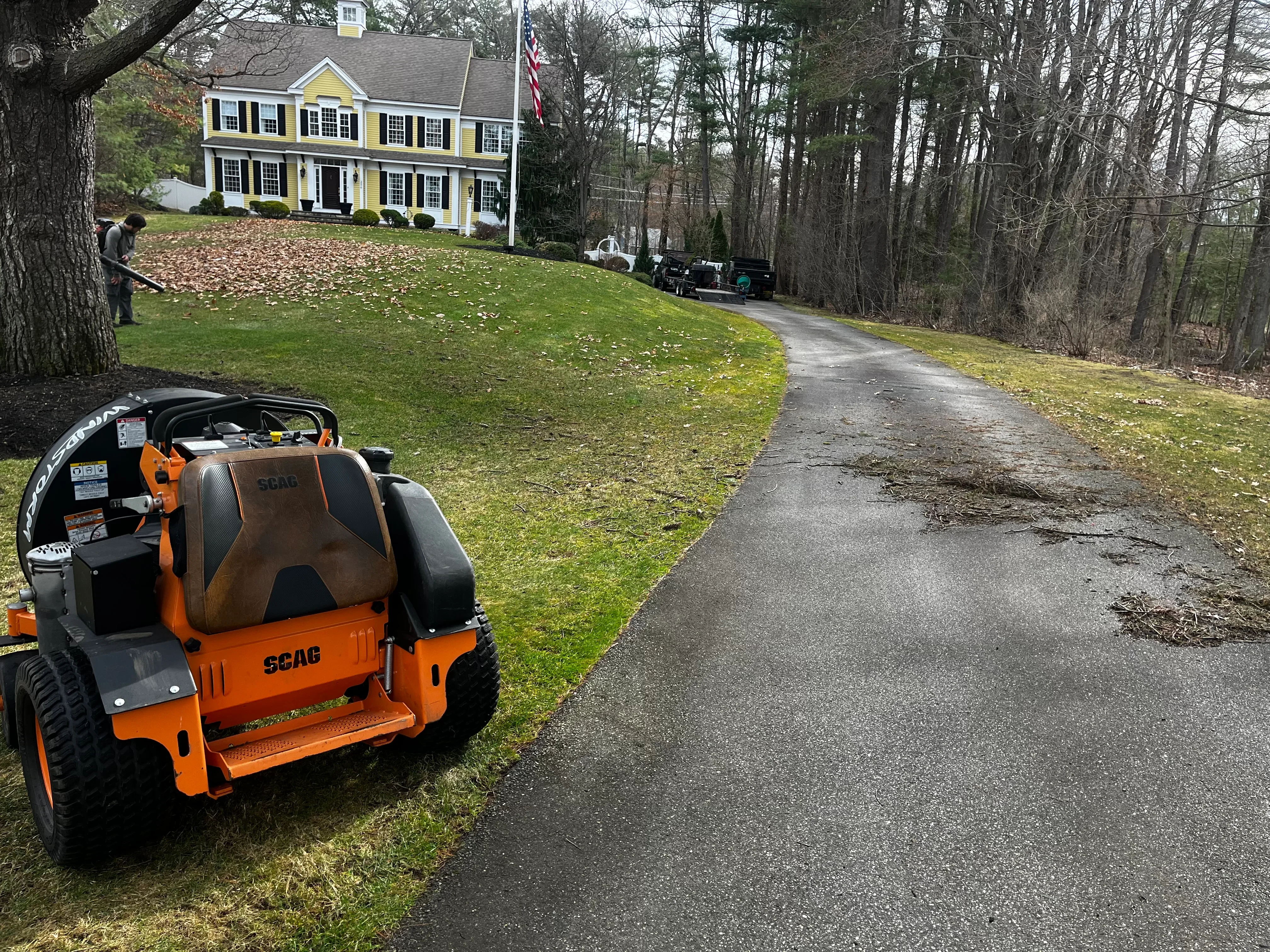 SCAC zero-turn mower on residential lawn with asphalt driveway and yellow colonial home in background