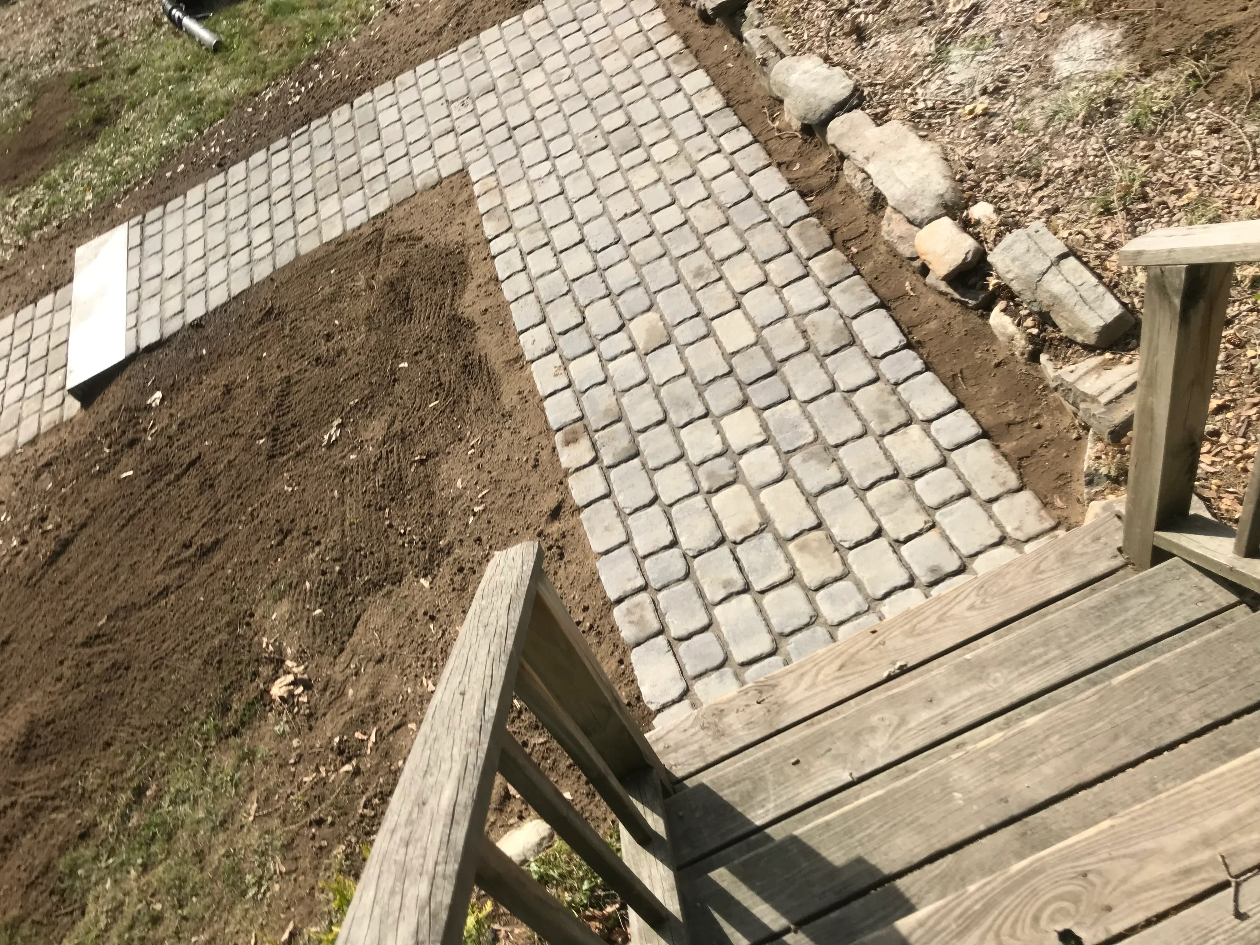 Permeable concrete pavers installed in grid pattern over gravel base with wooden deck edge