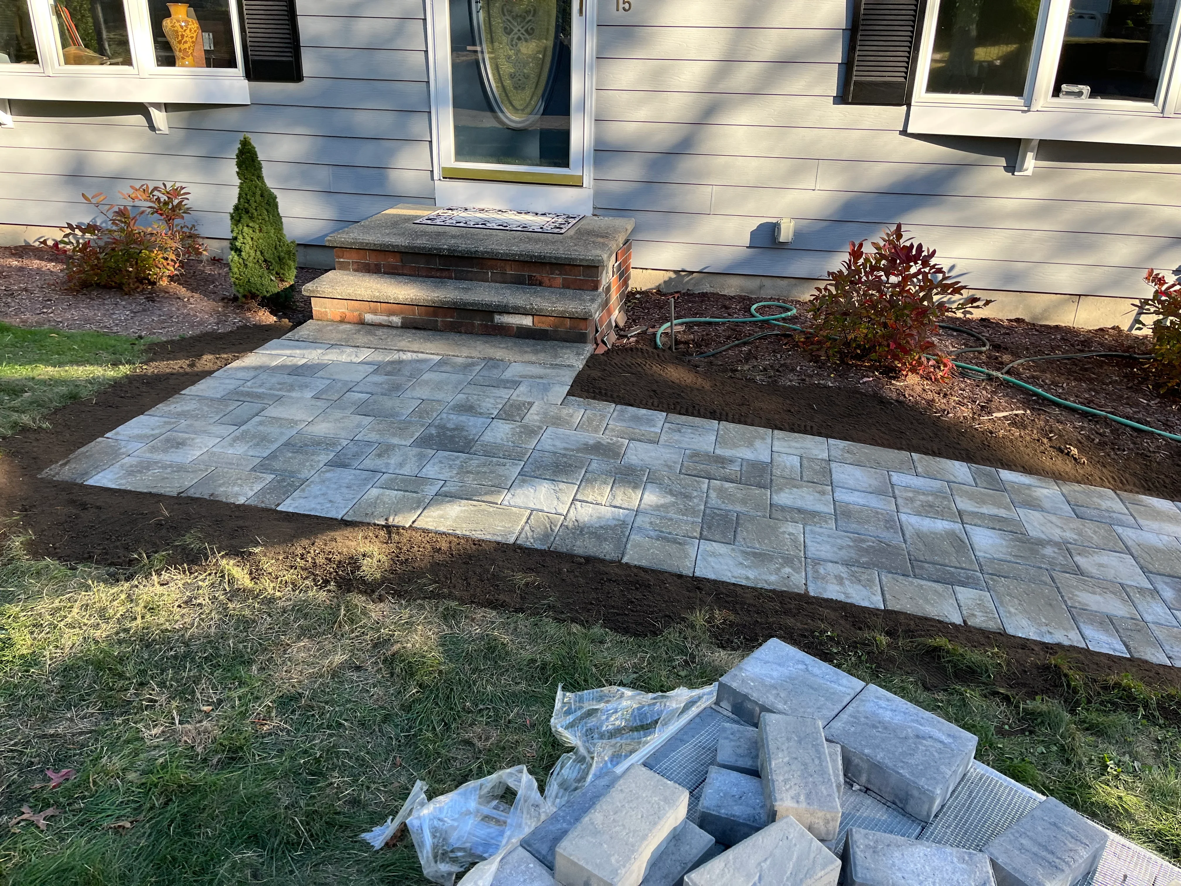 Gray concrete pavers in running bond pattern with brick entry steps and newly planted landscape beds