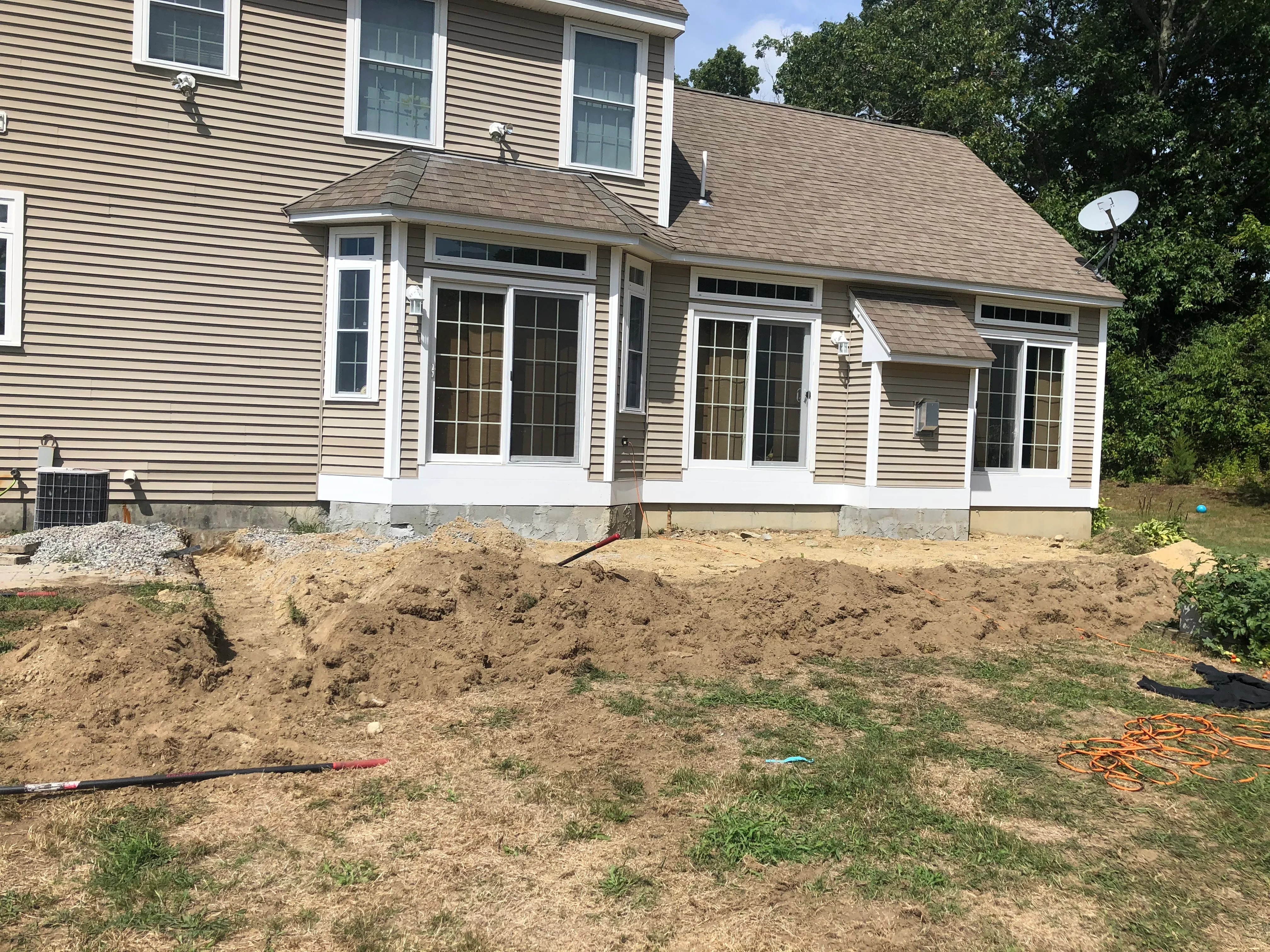 Graded dirt yard with excavation work in progress, vinyl-trimmed house addition visible