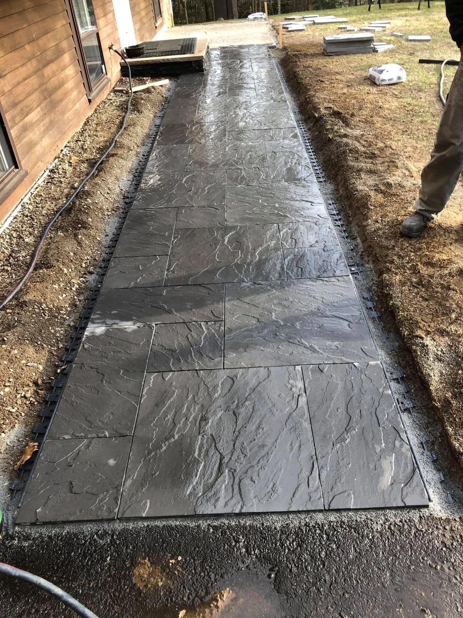 Dark slate pavers laid in running bond pattern along residential home foundation with gravel base