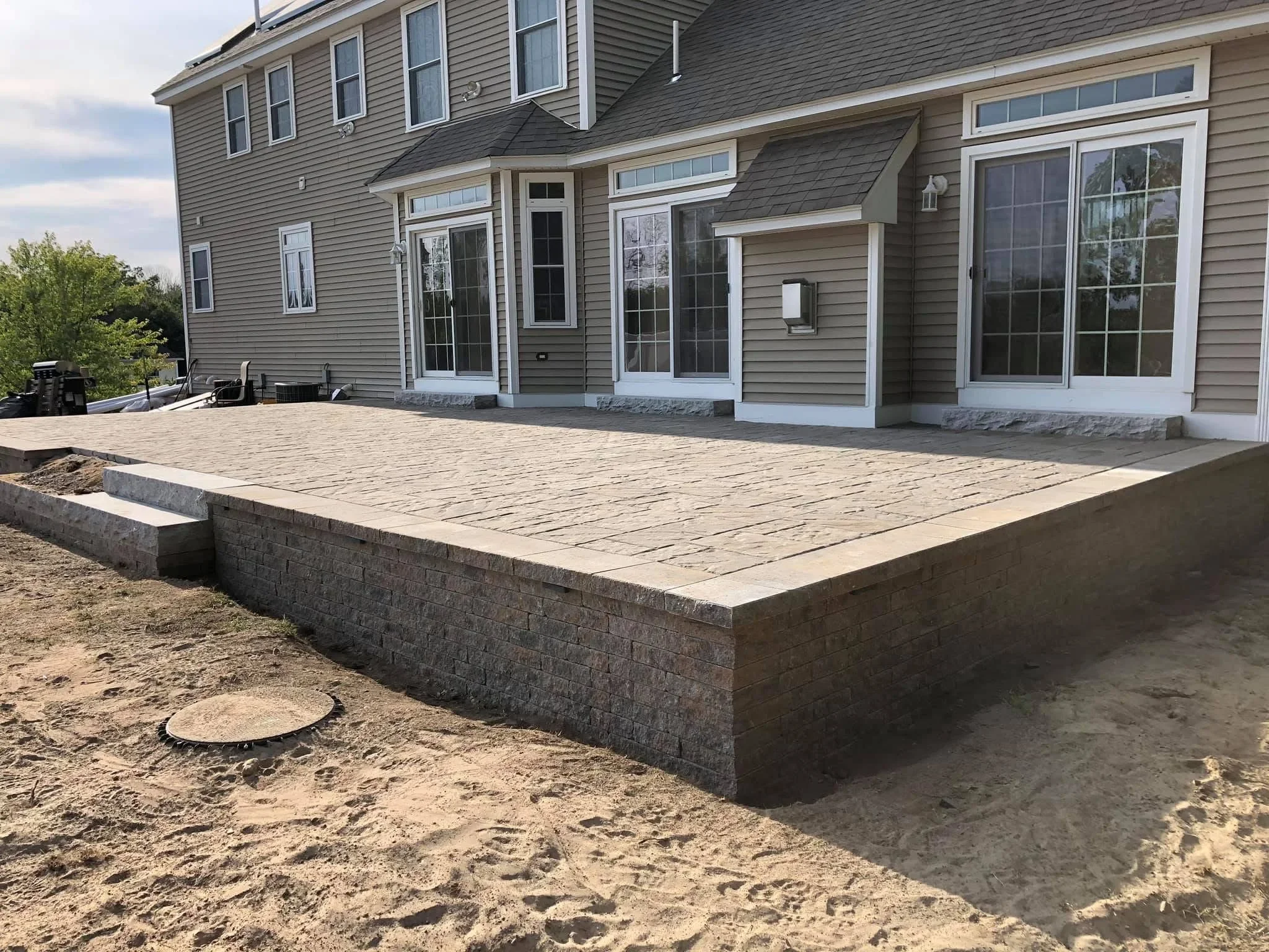 Raised paver patio with stacked stone retaining wall and concrete foundation