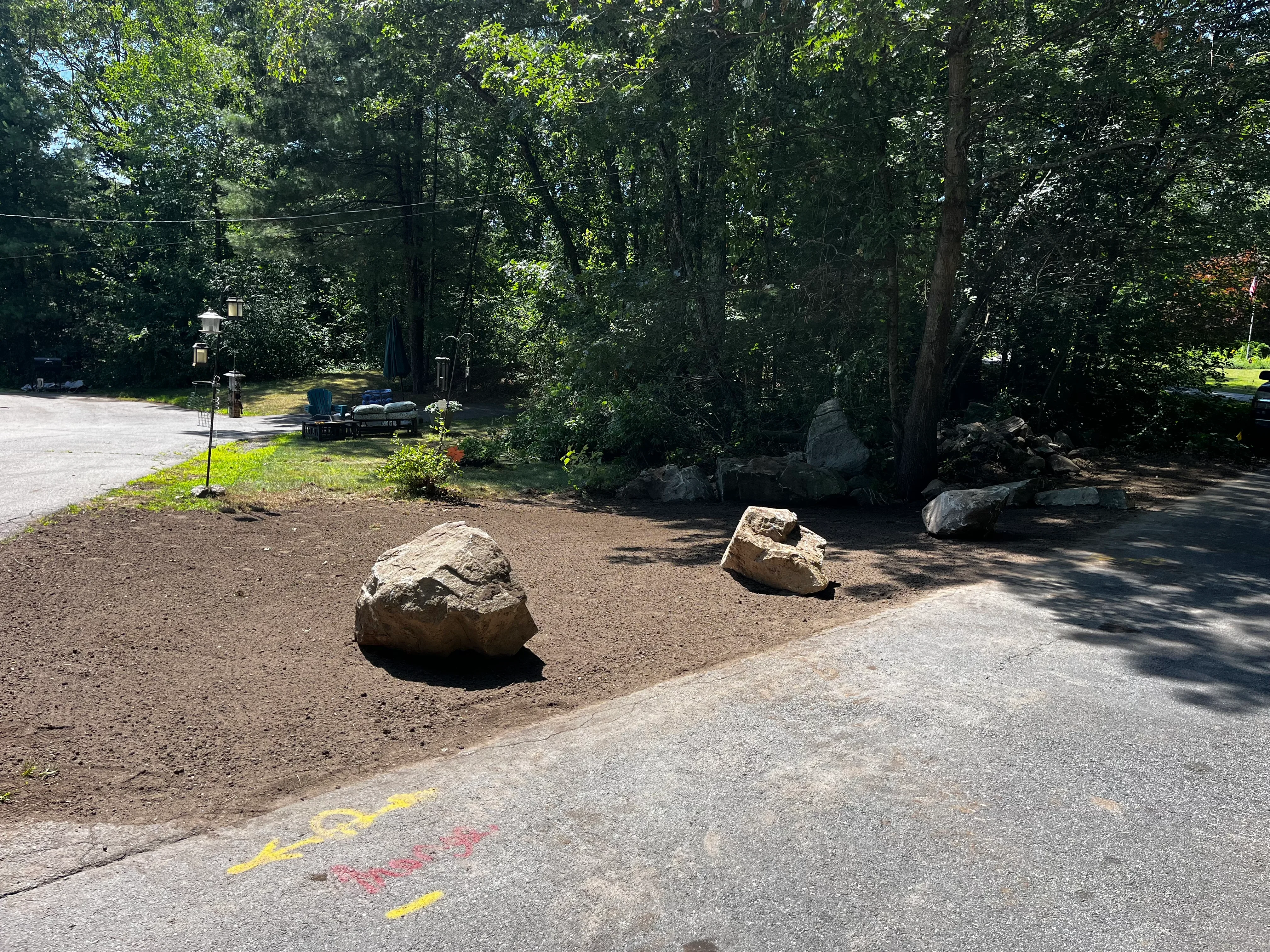 Large boulders placed in mulched woodland landscape with mature trees and driveway edge