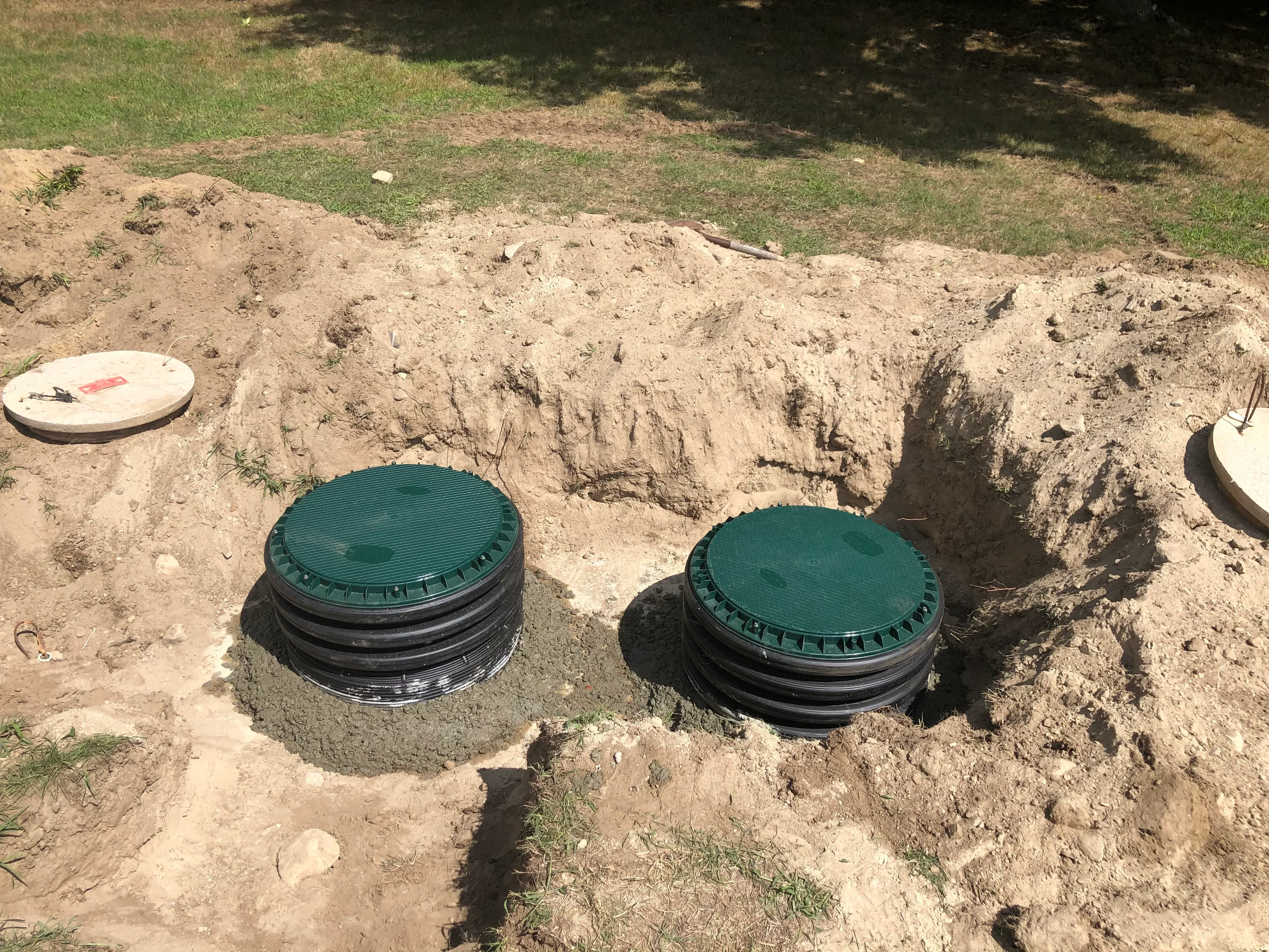 Two green-lidded septic tanks installed in excavated soil with surrounding earthwork and grass areas