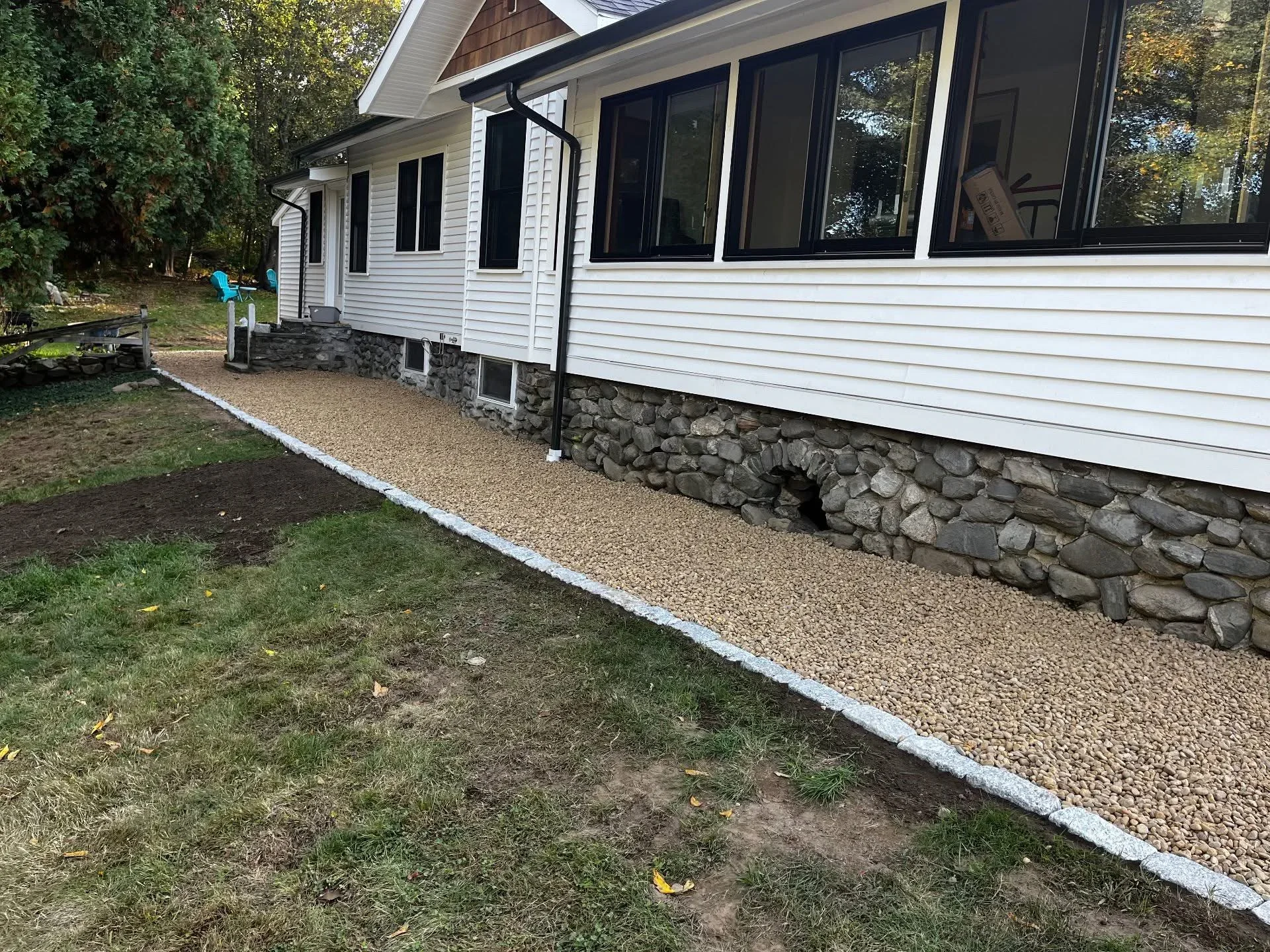 Gravel pathway with white edging and dry-stacked stone foundation wall along house