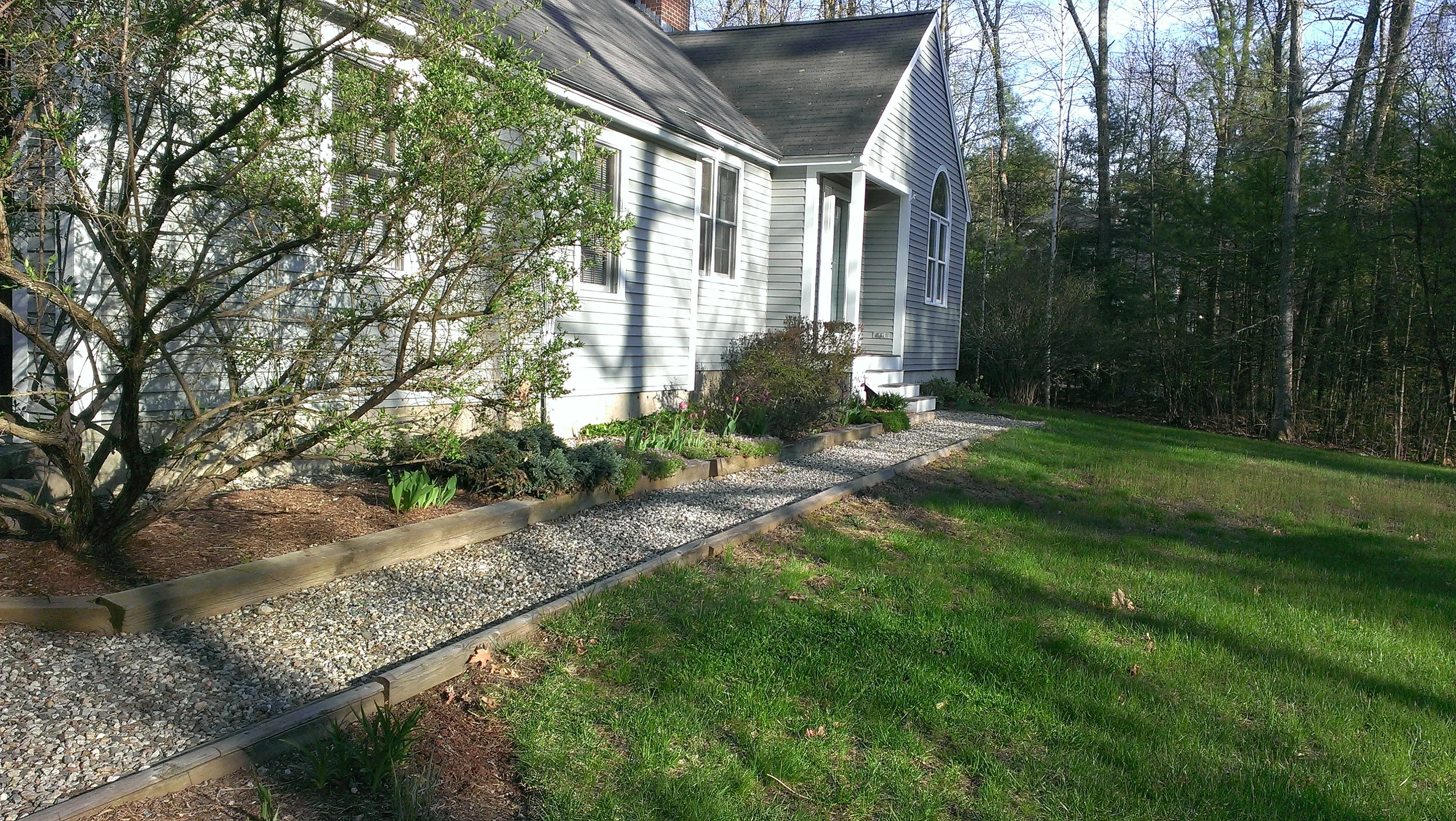 Gravel pathway with timber edging, planted beds, and mulch around home entrance