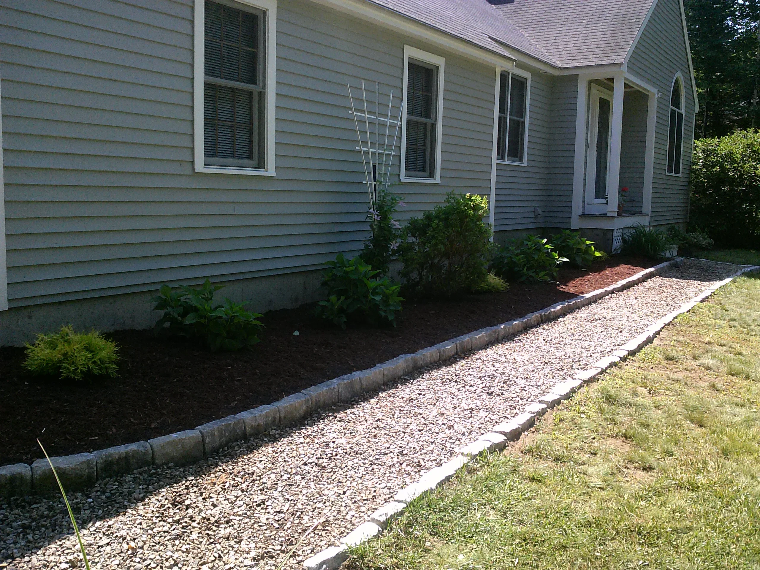 Foundation plantings with mulch beds, ornamental grasses, and stone edging along house exterior