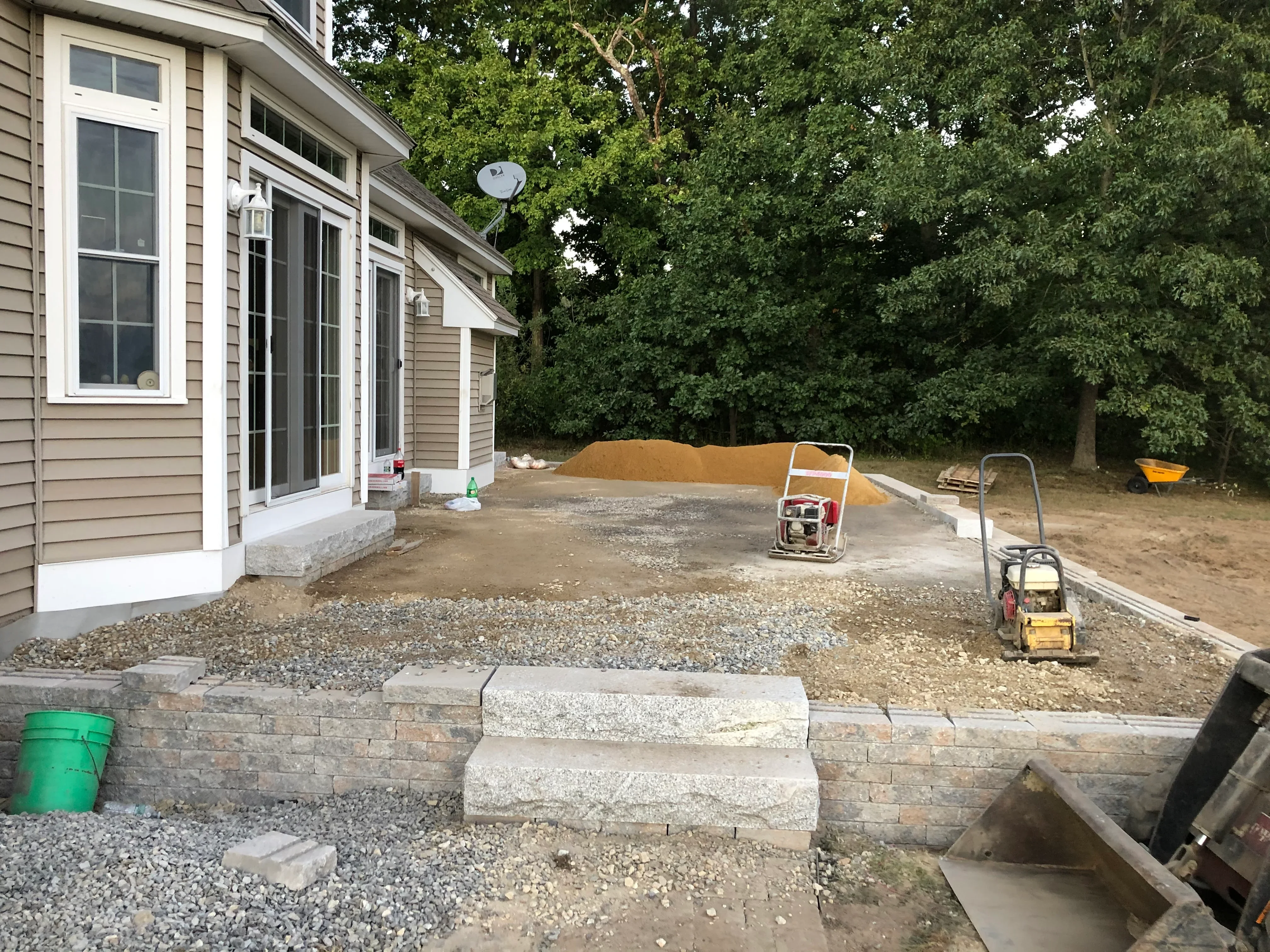 Stone retaining wall and gravel patio base under construction with concrete steps