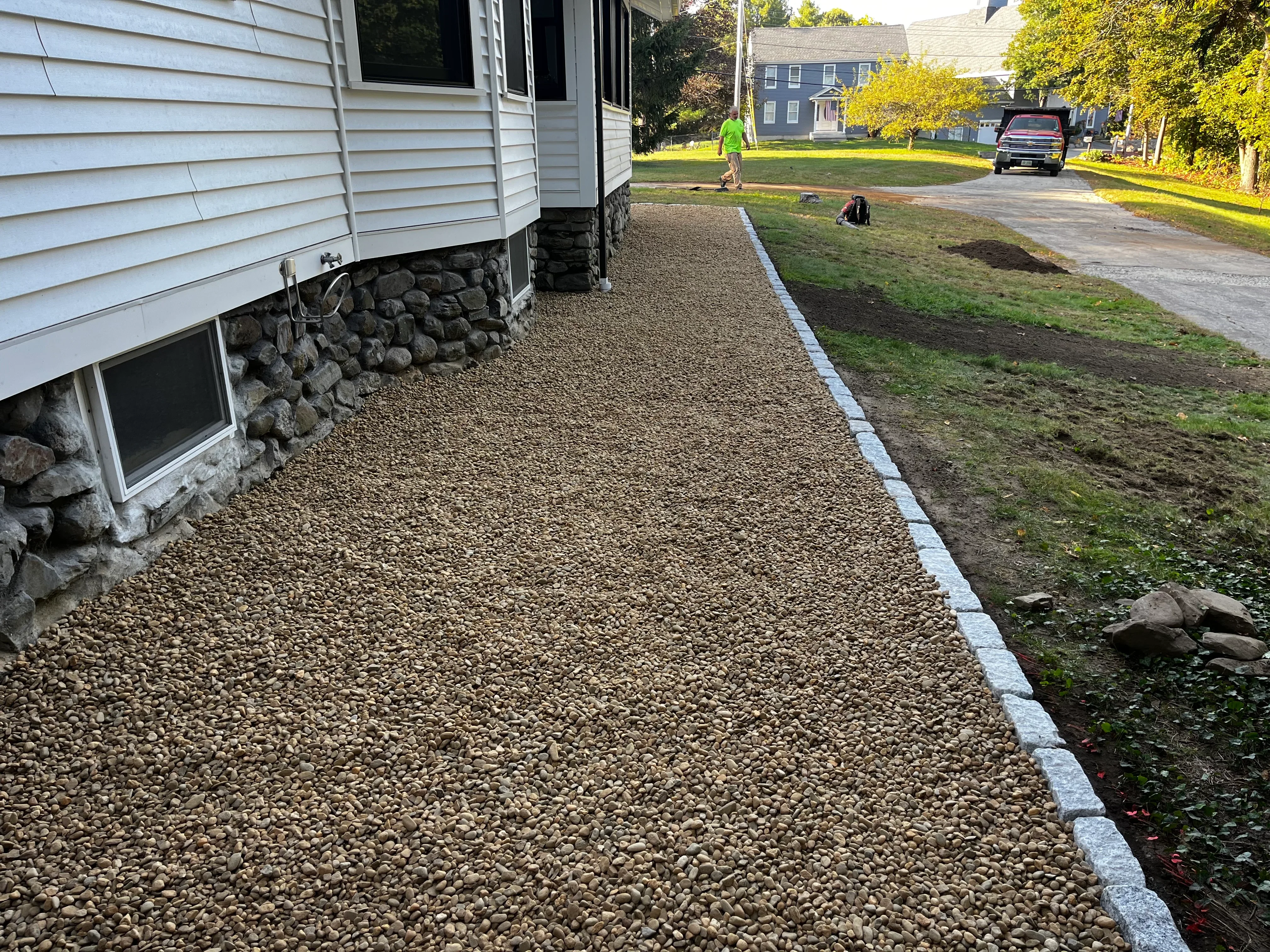 Gravel walkway with white stone edging along house foundation and stone retaining wall