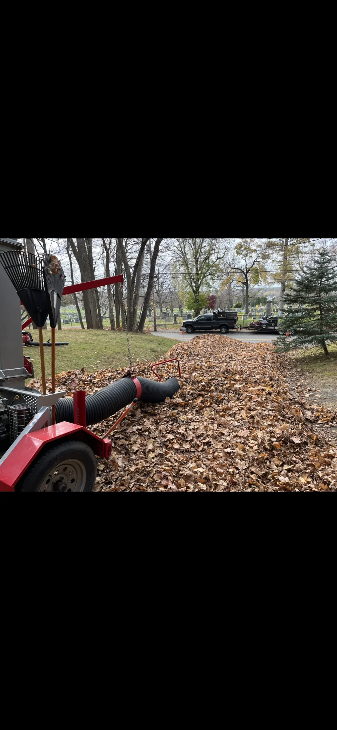 Red debris collection trailer with vacuum system removing leaves from wooded landscape