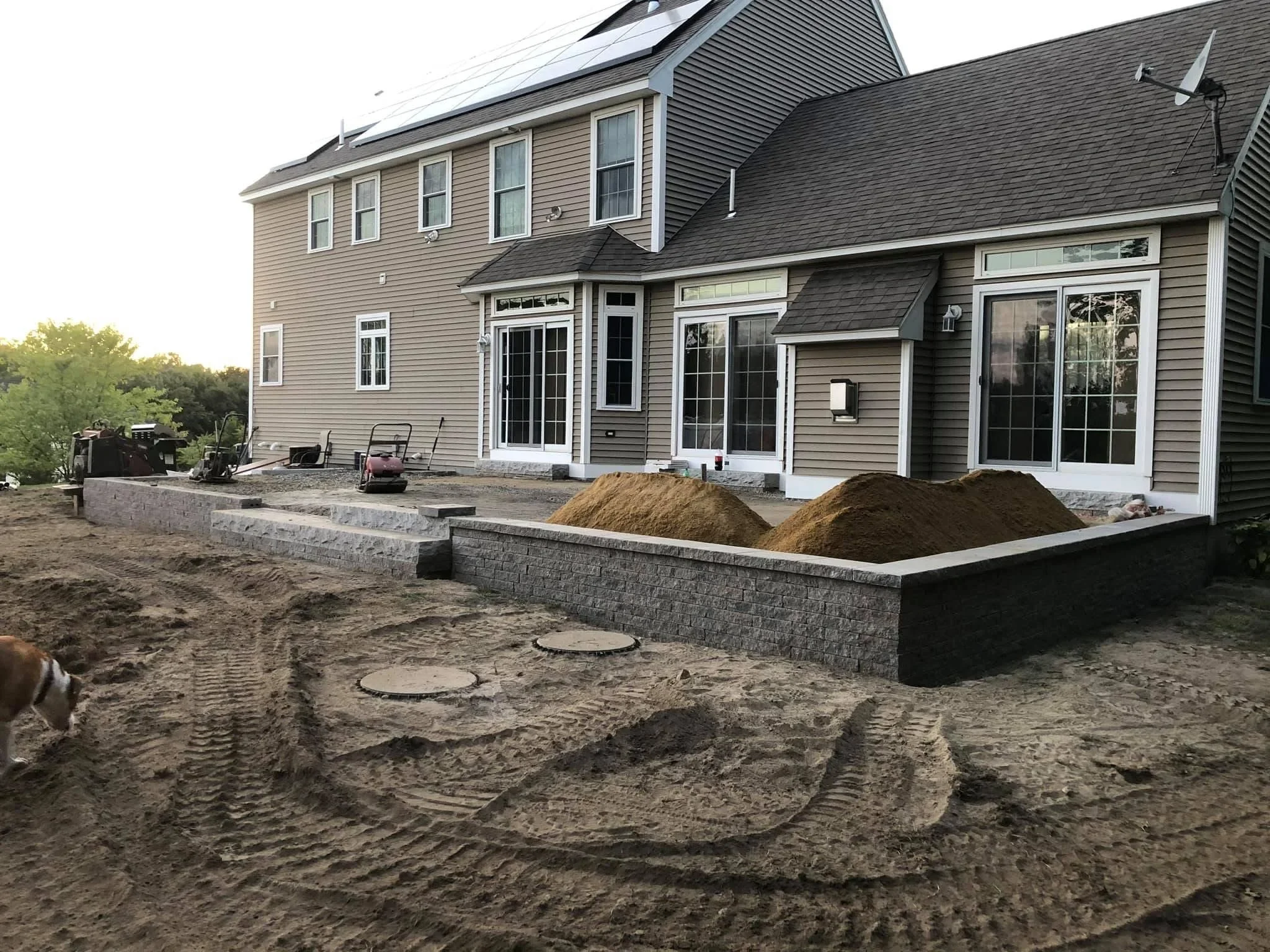 Stone retaining wall with white cap, planter beds, and graded soil during residential hardscape construction